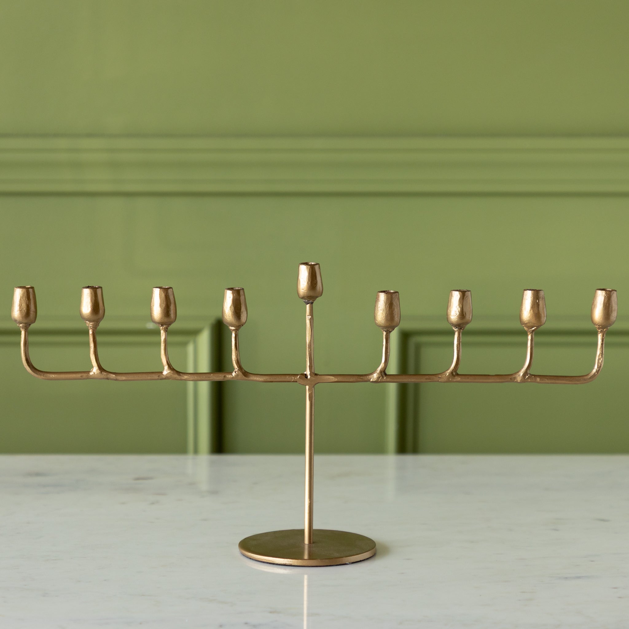 Gold menorah on a marble surface with a green wall background.