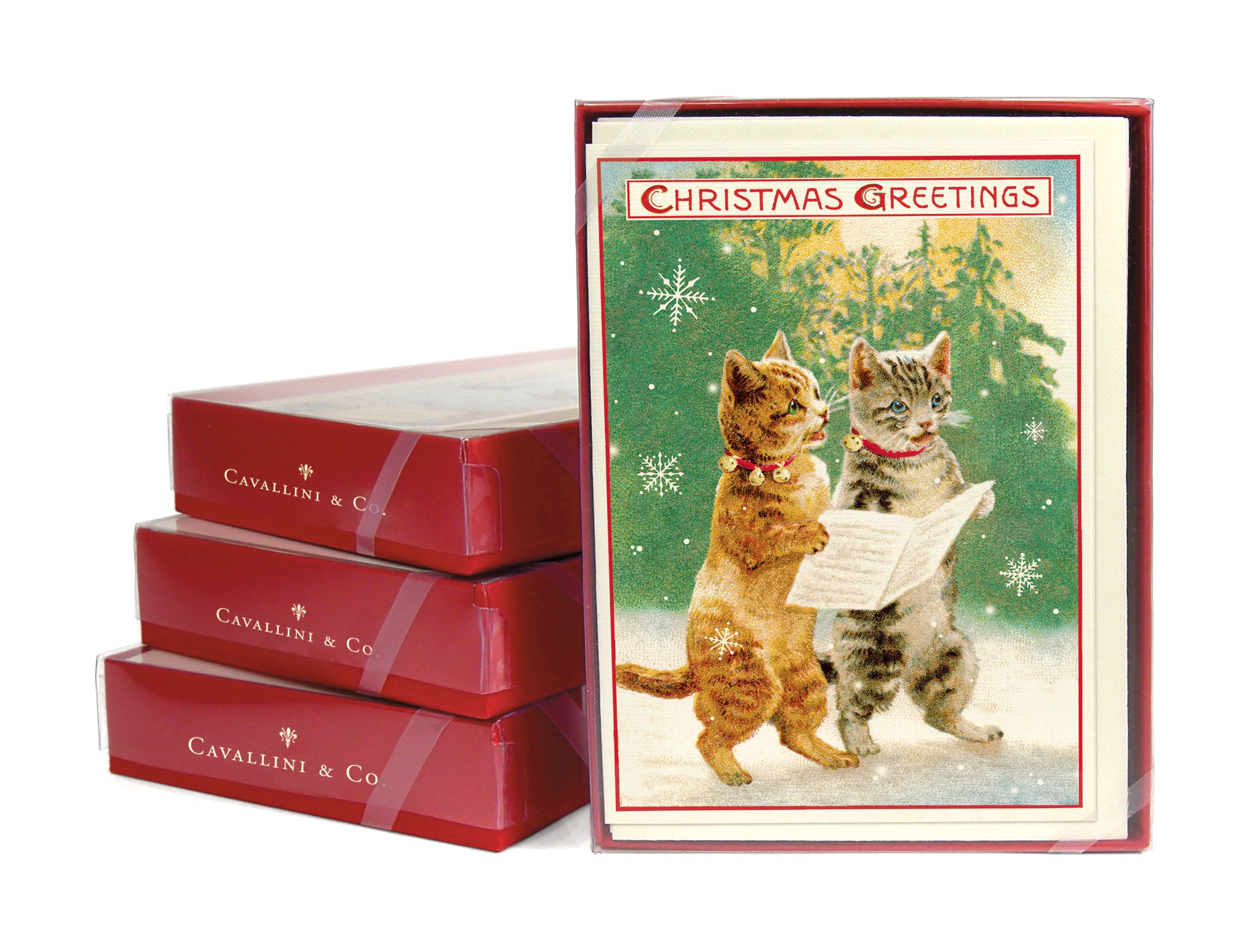 Three stacked card sets next to a front facing boxed card set of the Christmas Cats depicting two cats holding a paper in a snowy woods scene and "Christmas Greetings" at the top of the card.
