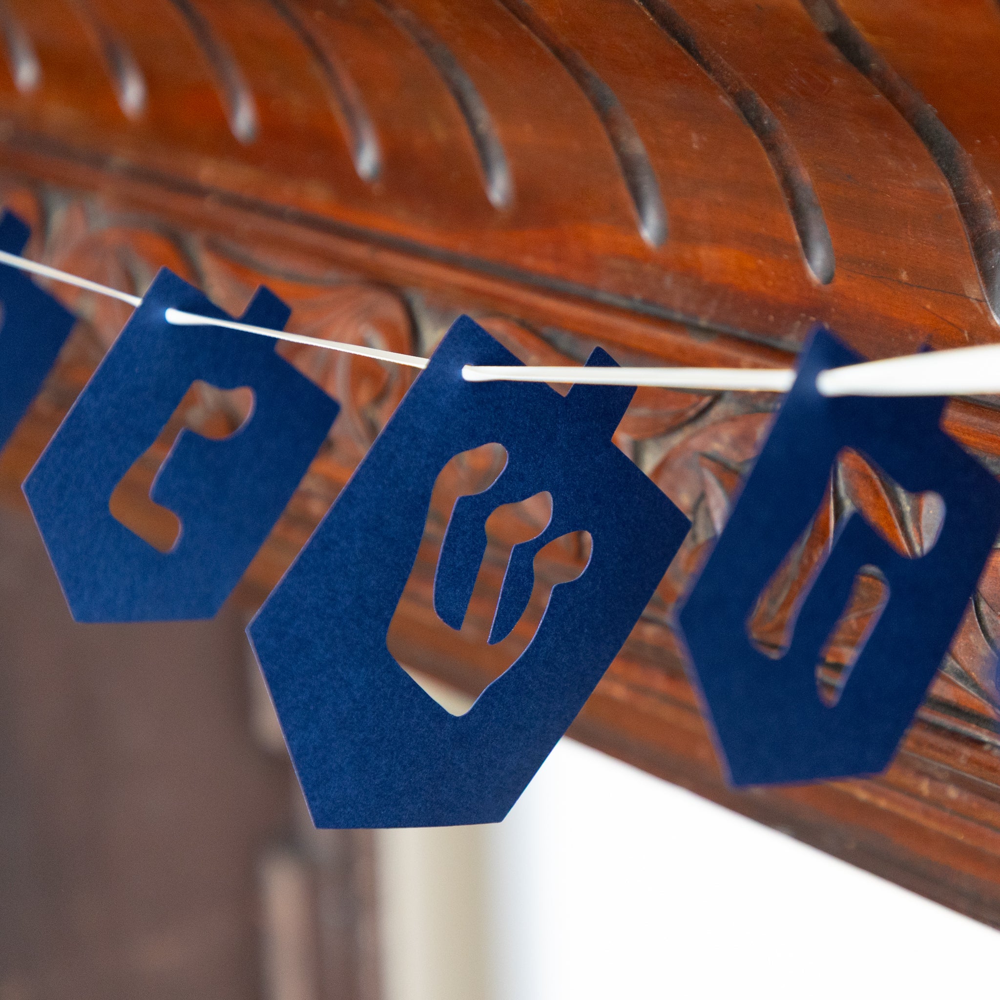 Blue paper dreidel garland on a string against a wooden background.