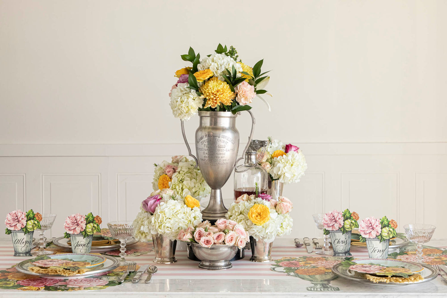 The Die-cut Garden Trophy Placemat in an elegant table setting for four, featuring a silver trophy in the floral centerpiece.
