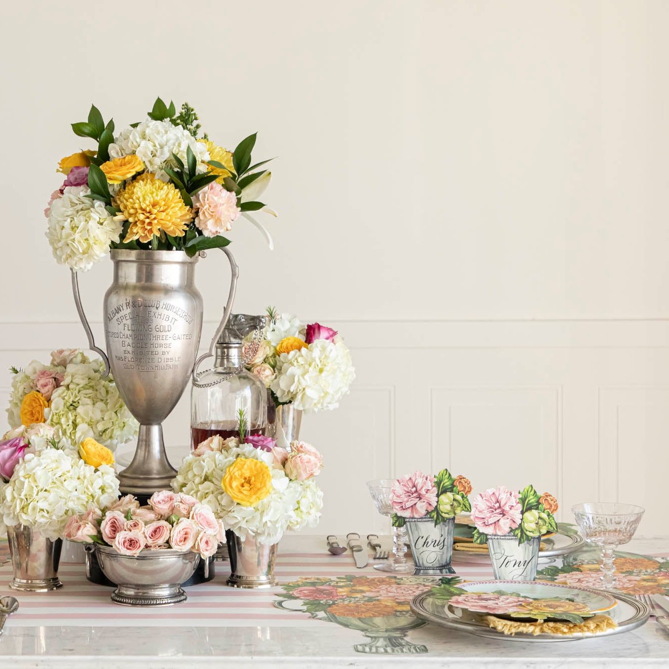 The Die-cut Garden Trophy Placemat in an elegant table setting for four, featuring a silver trophy in the floral centerpiece.