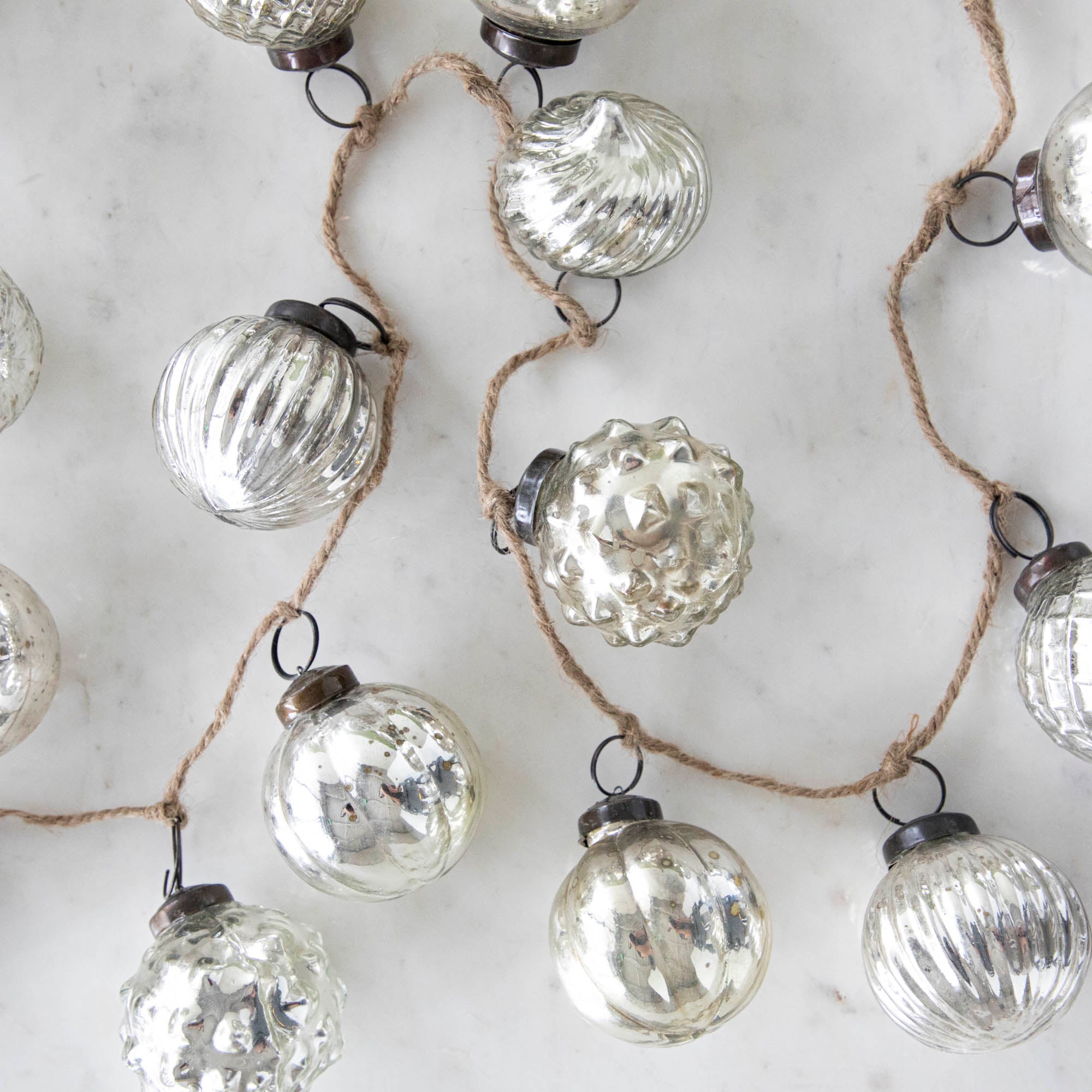 Silver Embossed Mercury Glass Ornament Garland with a jute cord on a marble table.