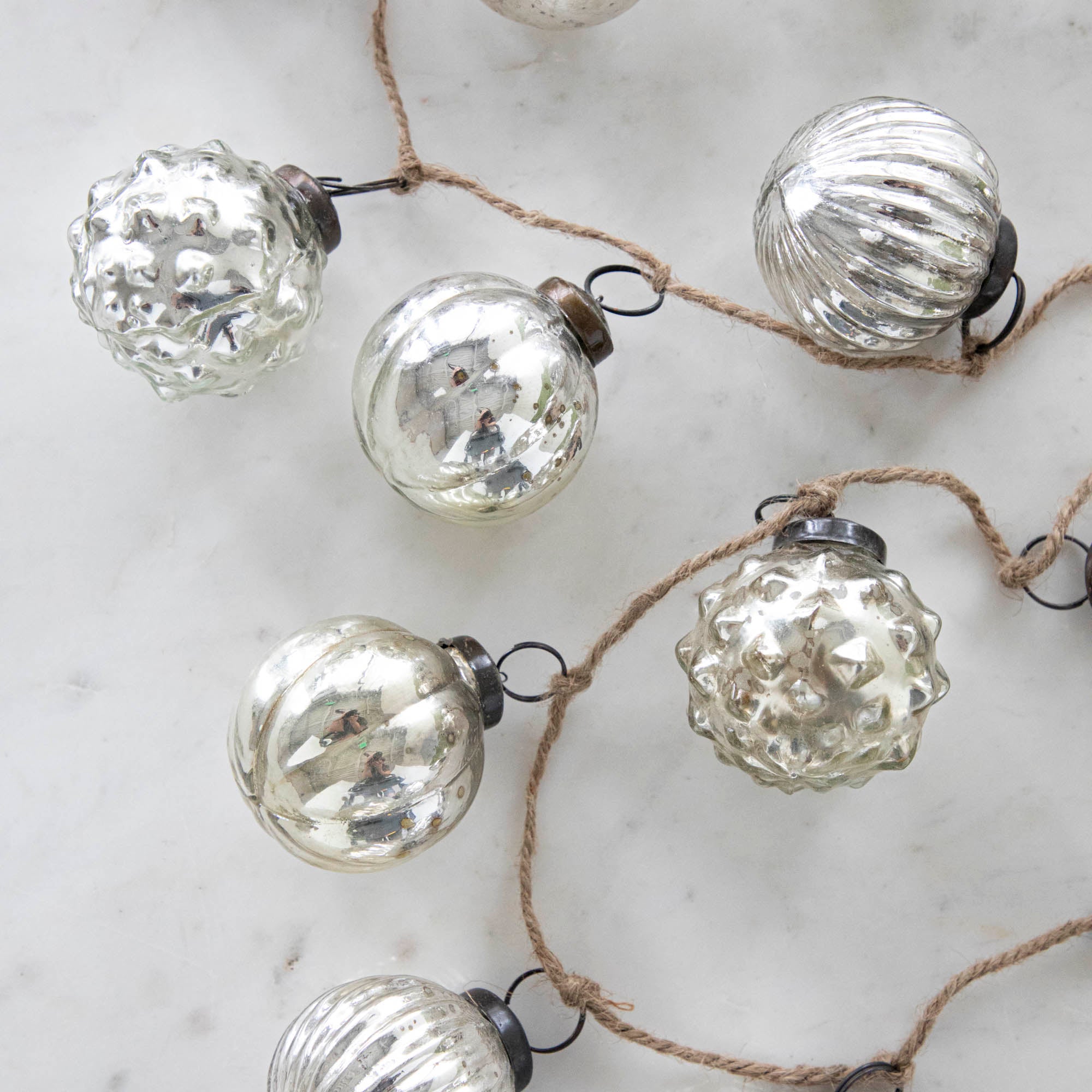 Silver Embossed Mercury Glass Ornament Garland with a jute cord on a marble table.
