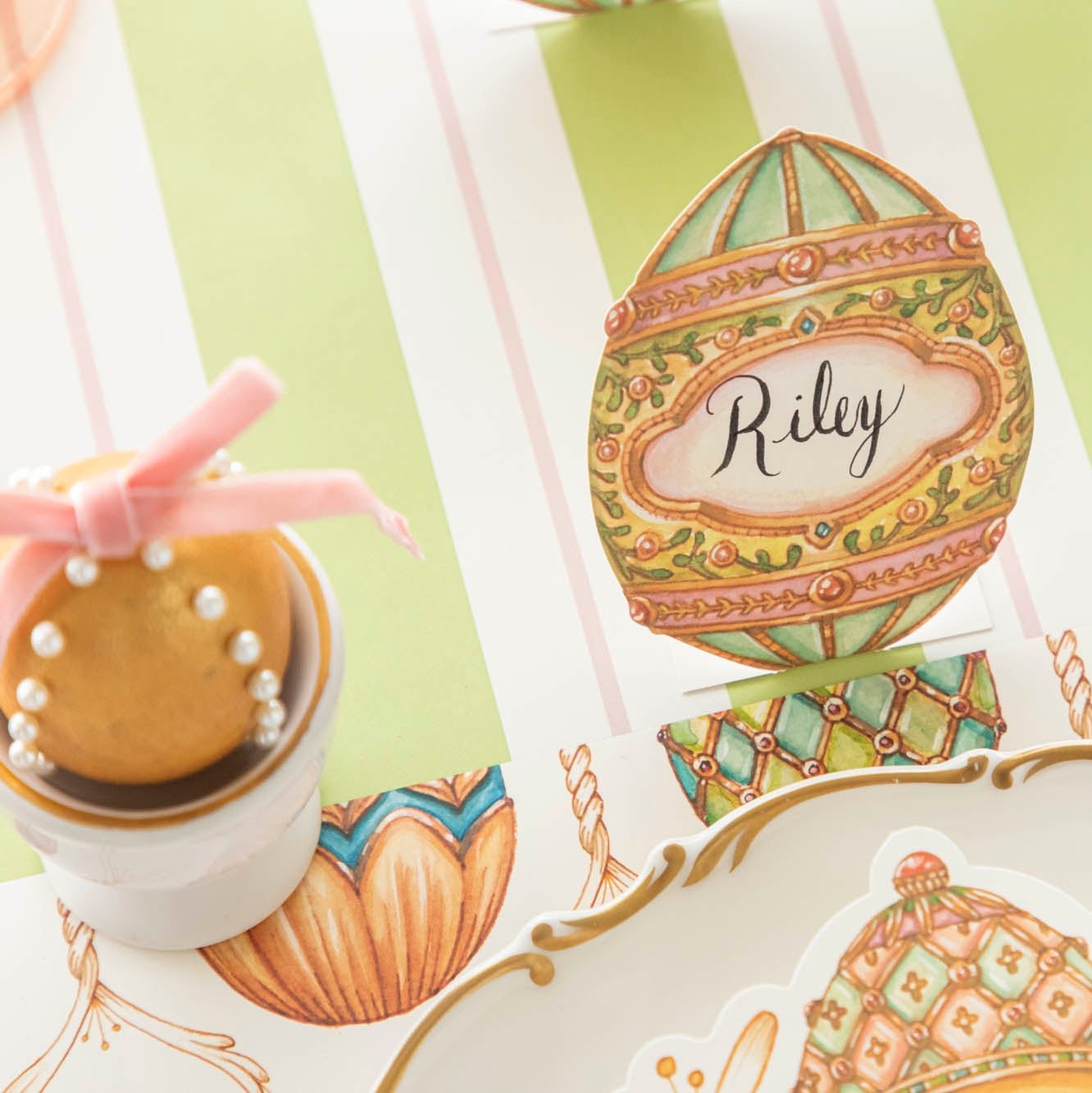 The Exquisite Egg Place Card with "Riley" written on it, next to a decorated egg, on an elegant table setting.
