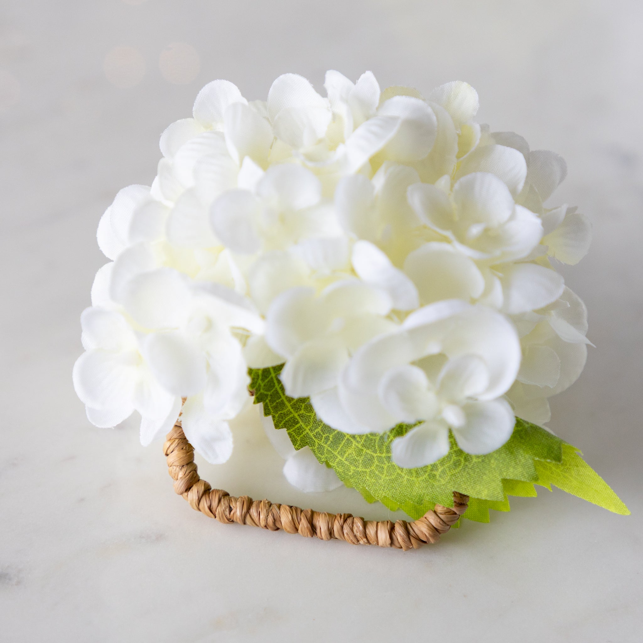 Cream Hydrangea Napkin Ring with a rattan ring on a marble surface.