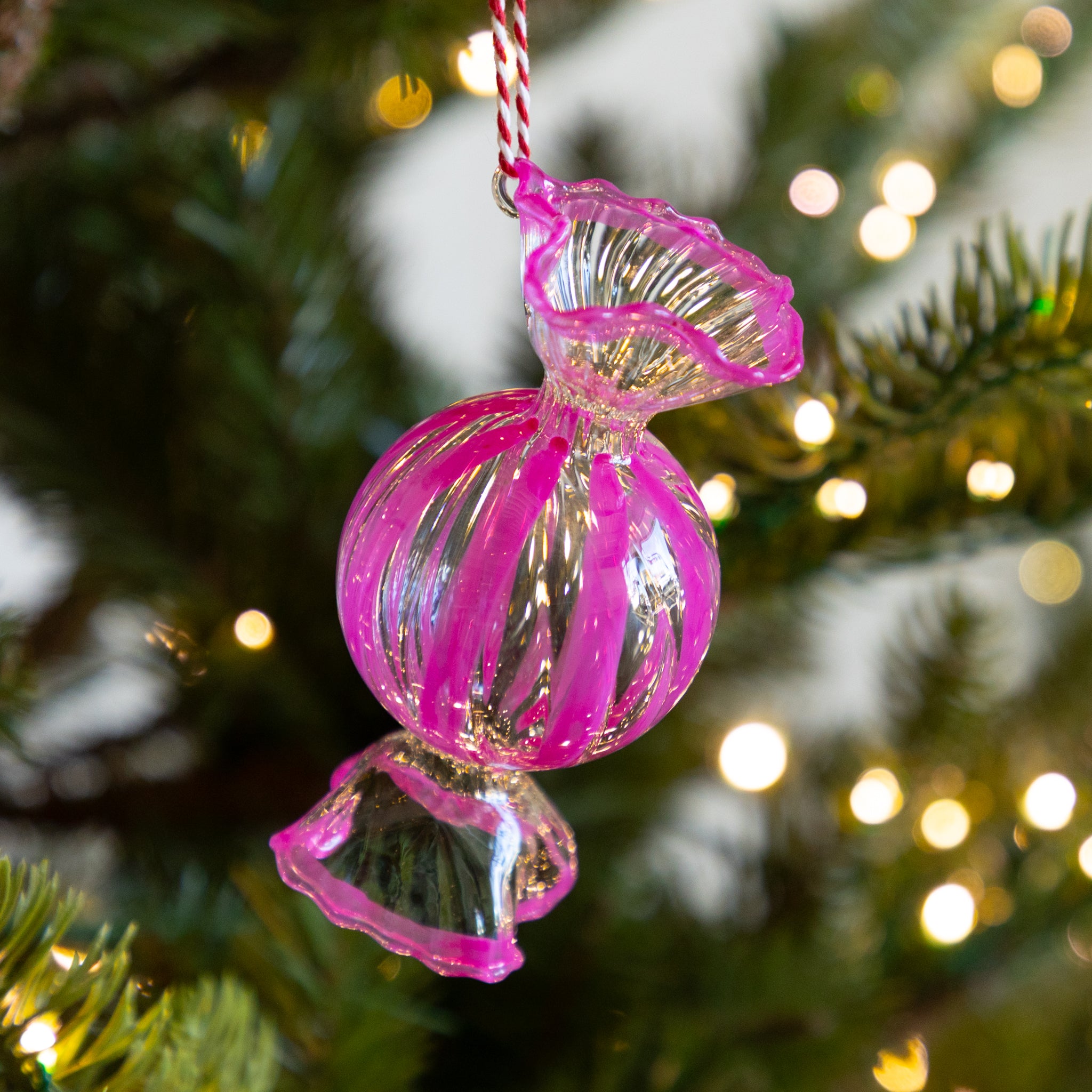 Round, dark pink glass candy ornament hanging on a Christmas tree with blurred lights in the background.