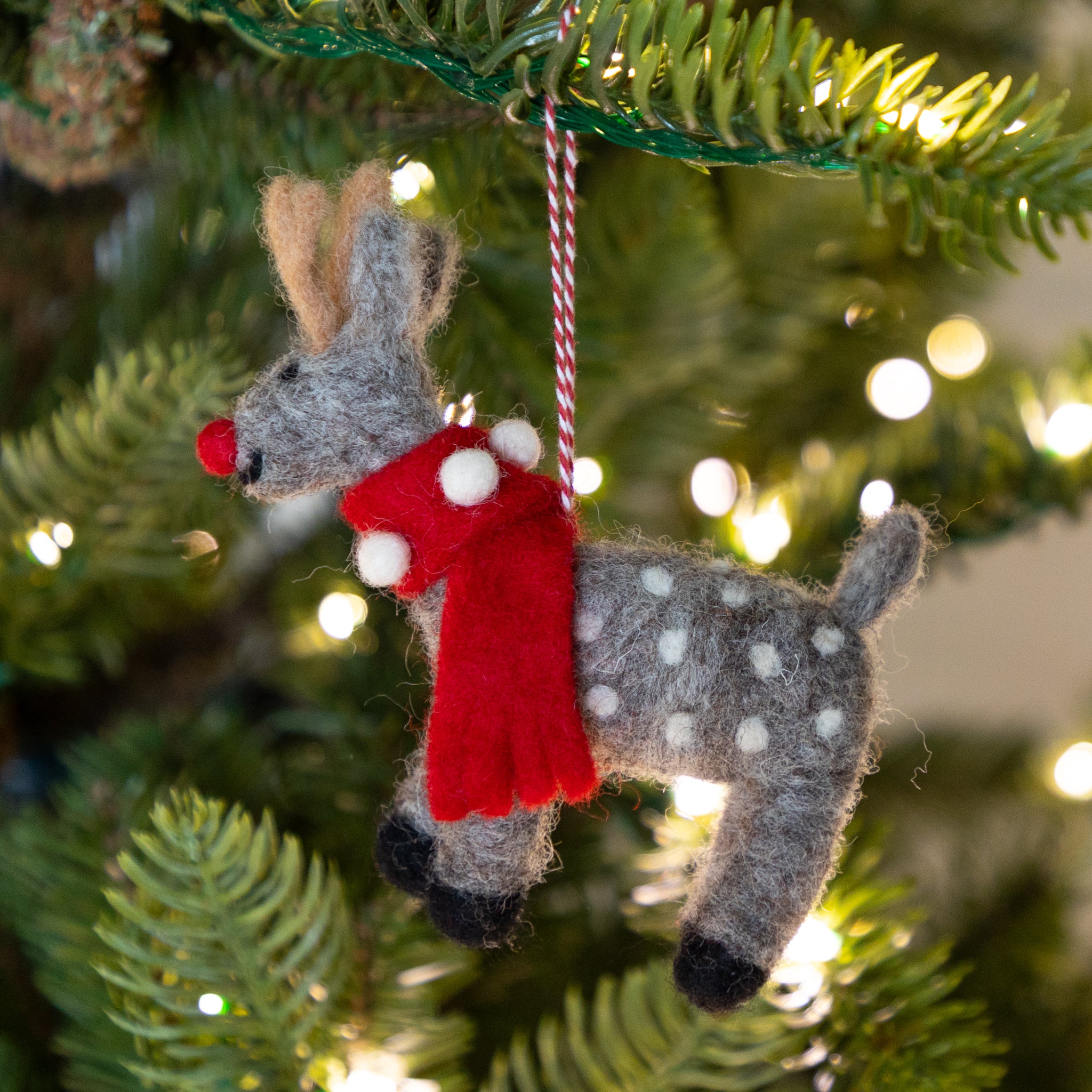 Felt deer ornament in gray with white spots and a red scarf hanging on a Christmas tree.