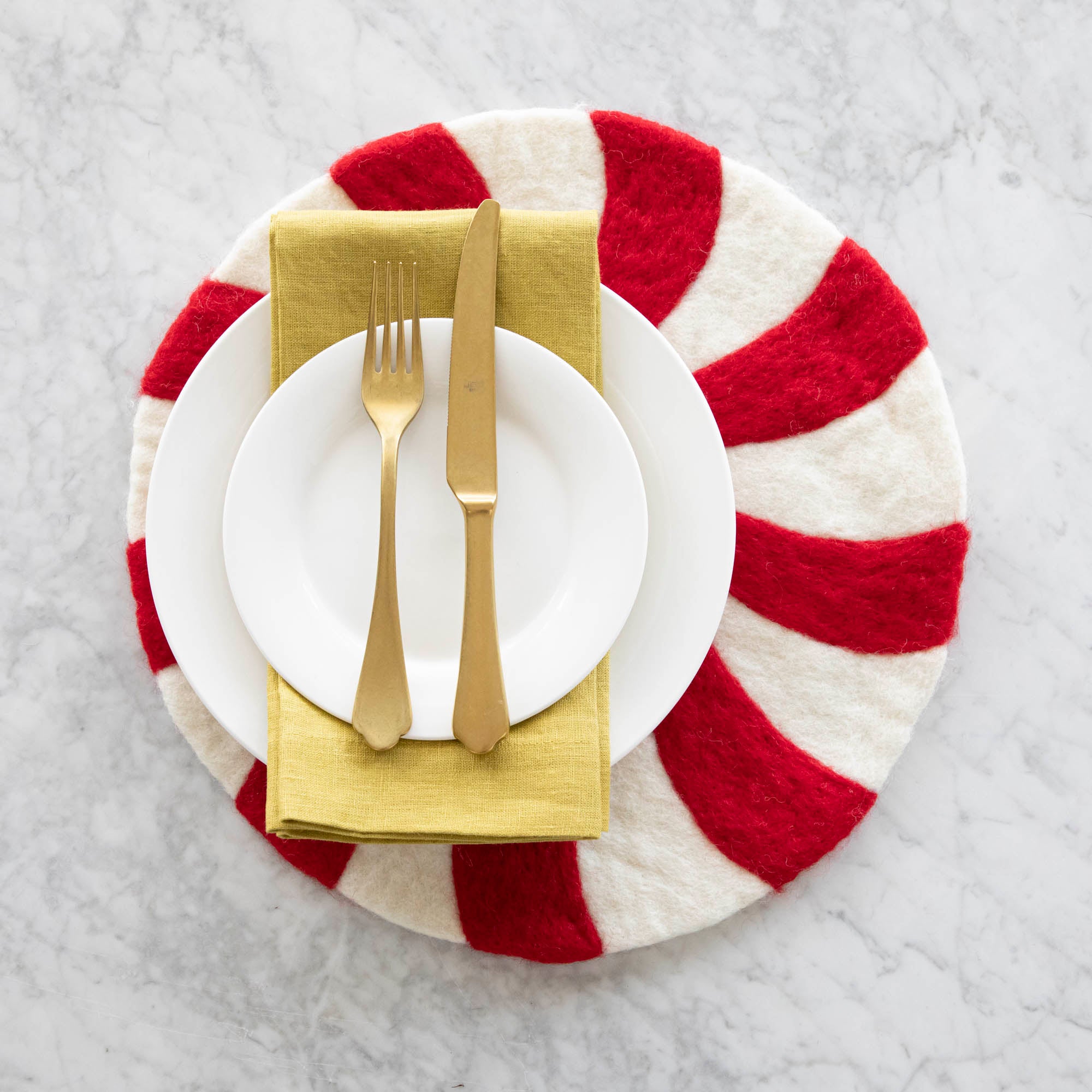 The Red Felt Candy Stripe Placemat under a place setting with two white plates, a gold napkin and a gold fork and knife.