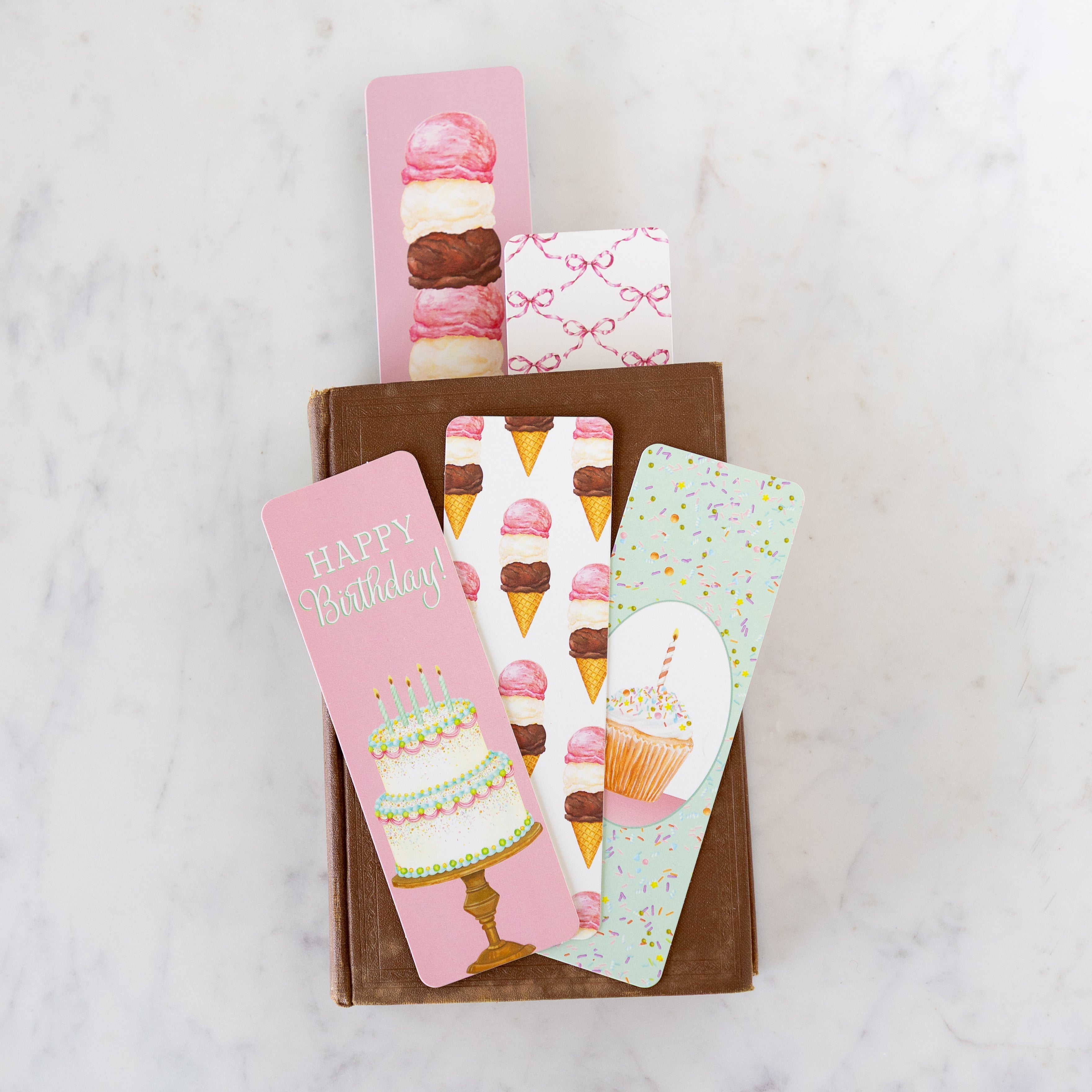 A brown book with a Ice Cream Party and Pink Bow bookmark sticking out the inside, with a Happy Birthday and two Ice Cream Party bookmarks atop.