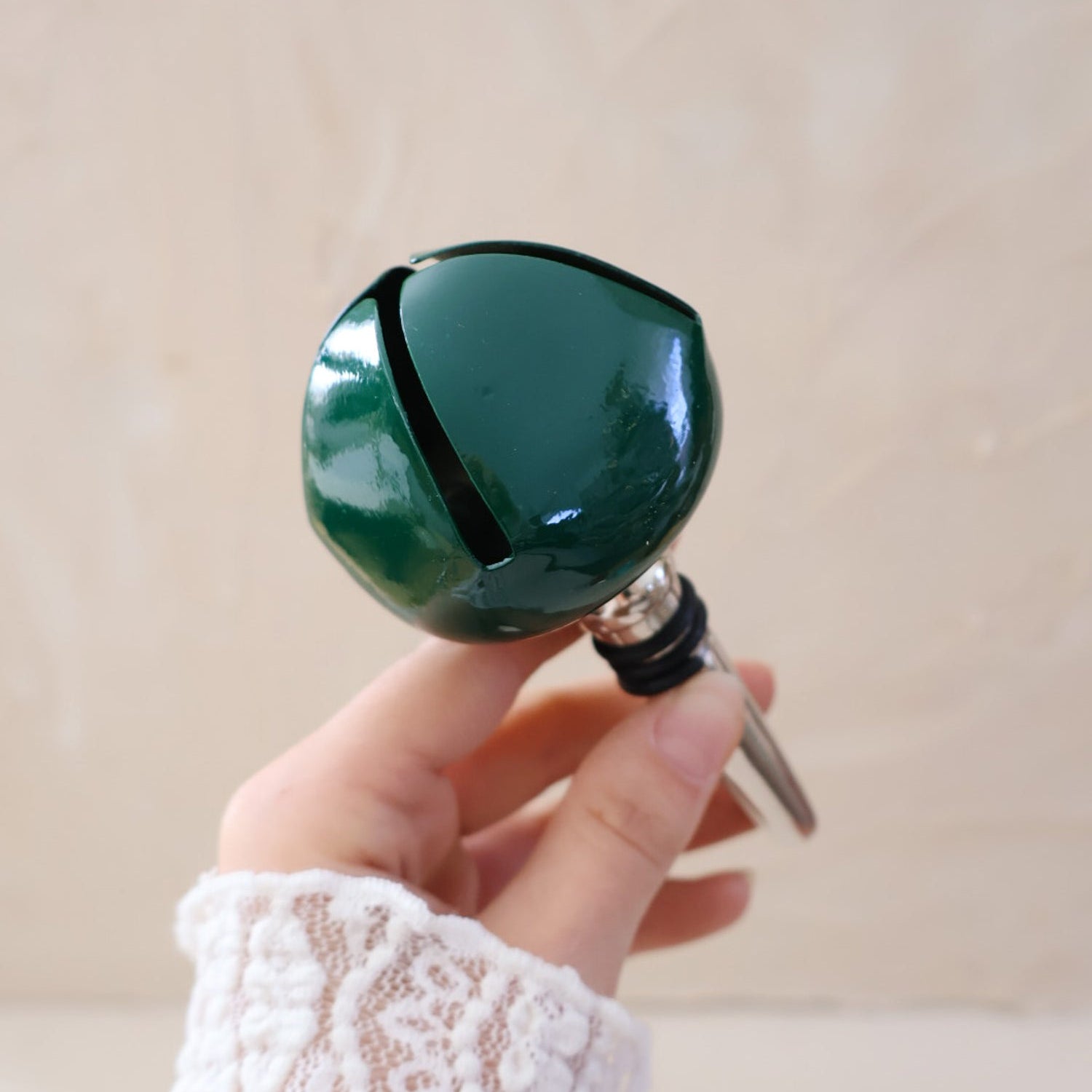 Hand holding a green bell bottle stopper against a beige background.