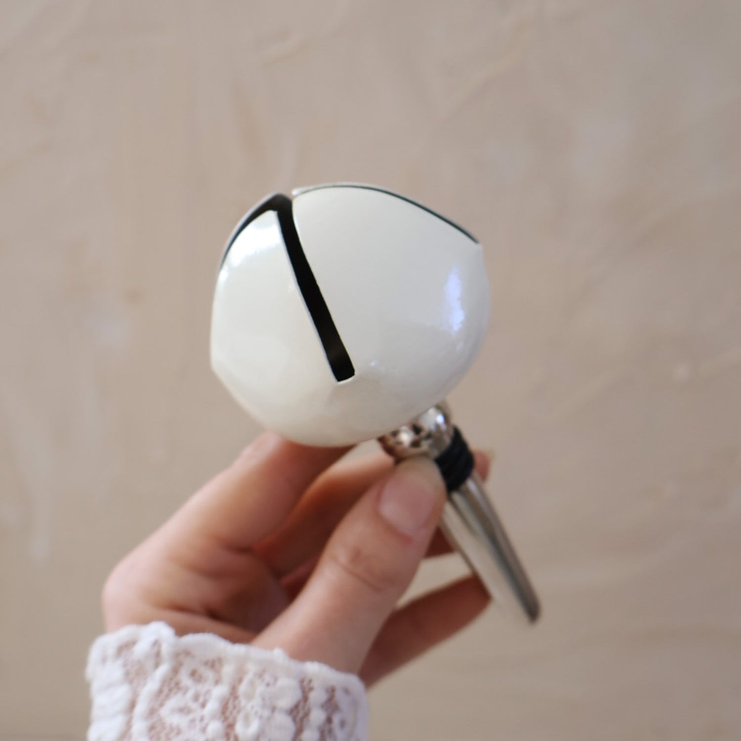 White bell bottle stopper held by a hand against a beige background.