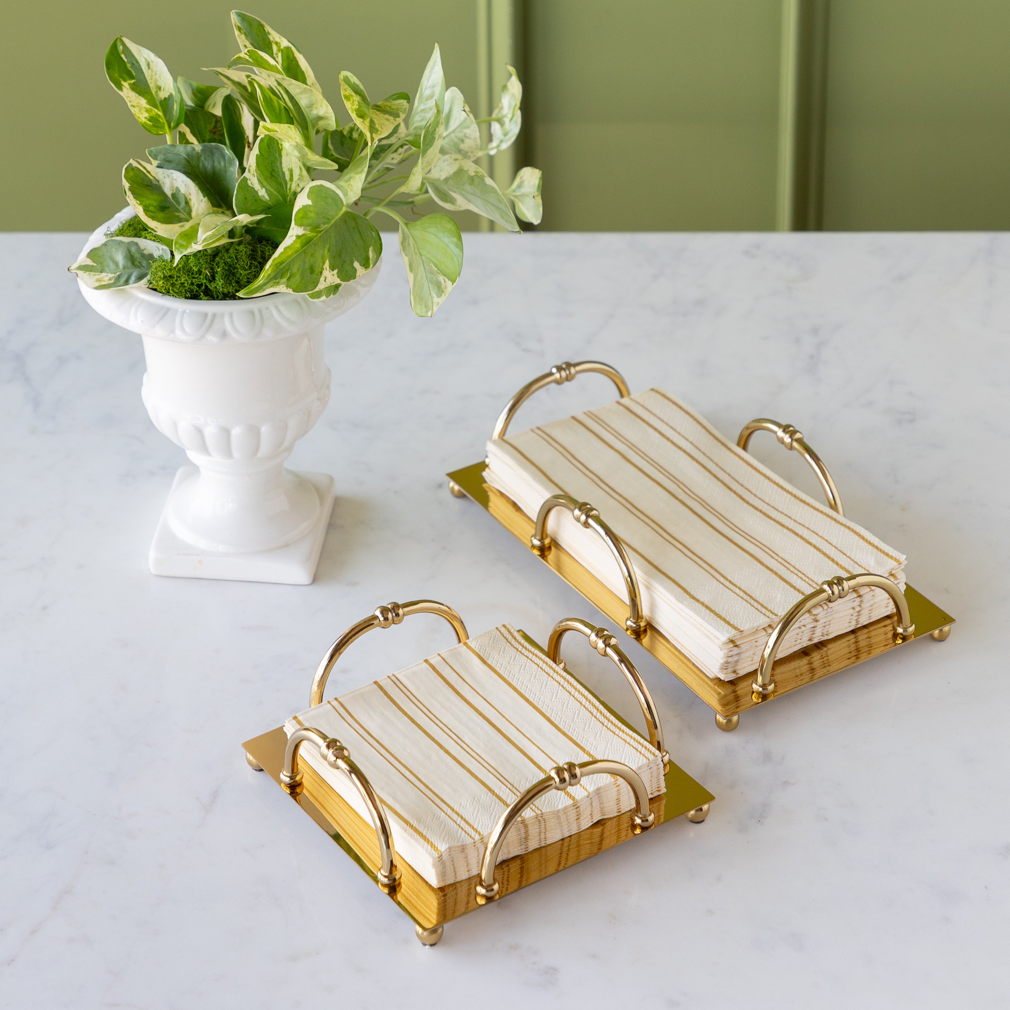 Gold Scalloped Napkin Holders with Antique Gold Stripe Napkins in them, on a marble table with a potted plant.