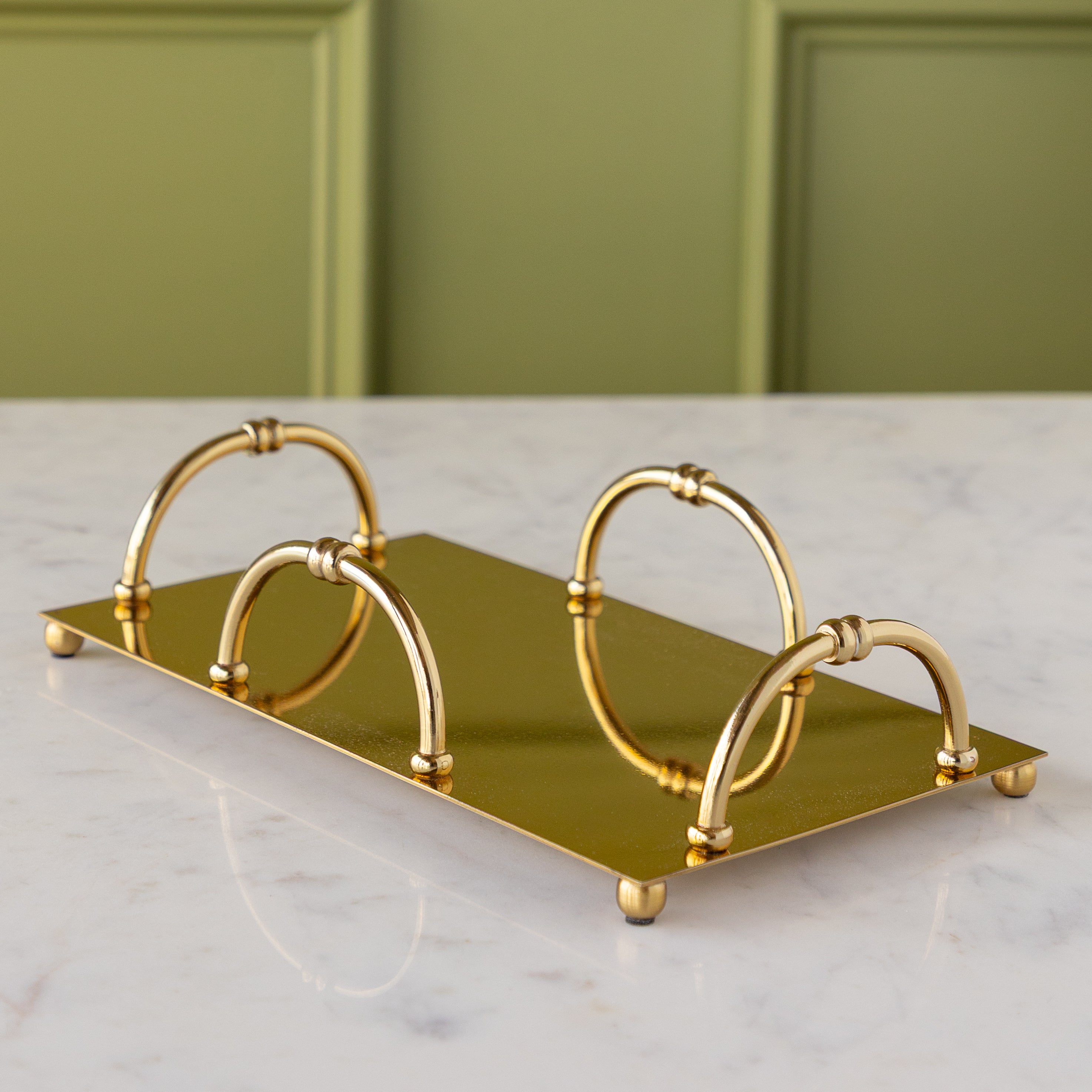 A gold rectangular metal napkin holder with four arched handles sits on a white marble surface.