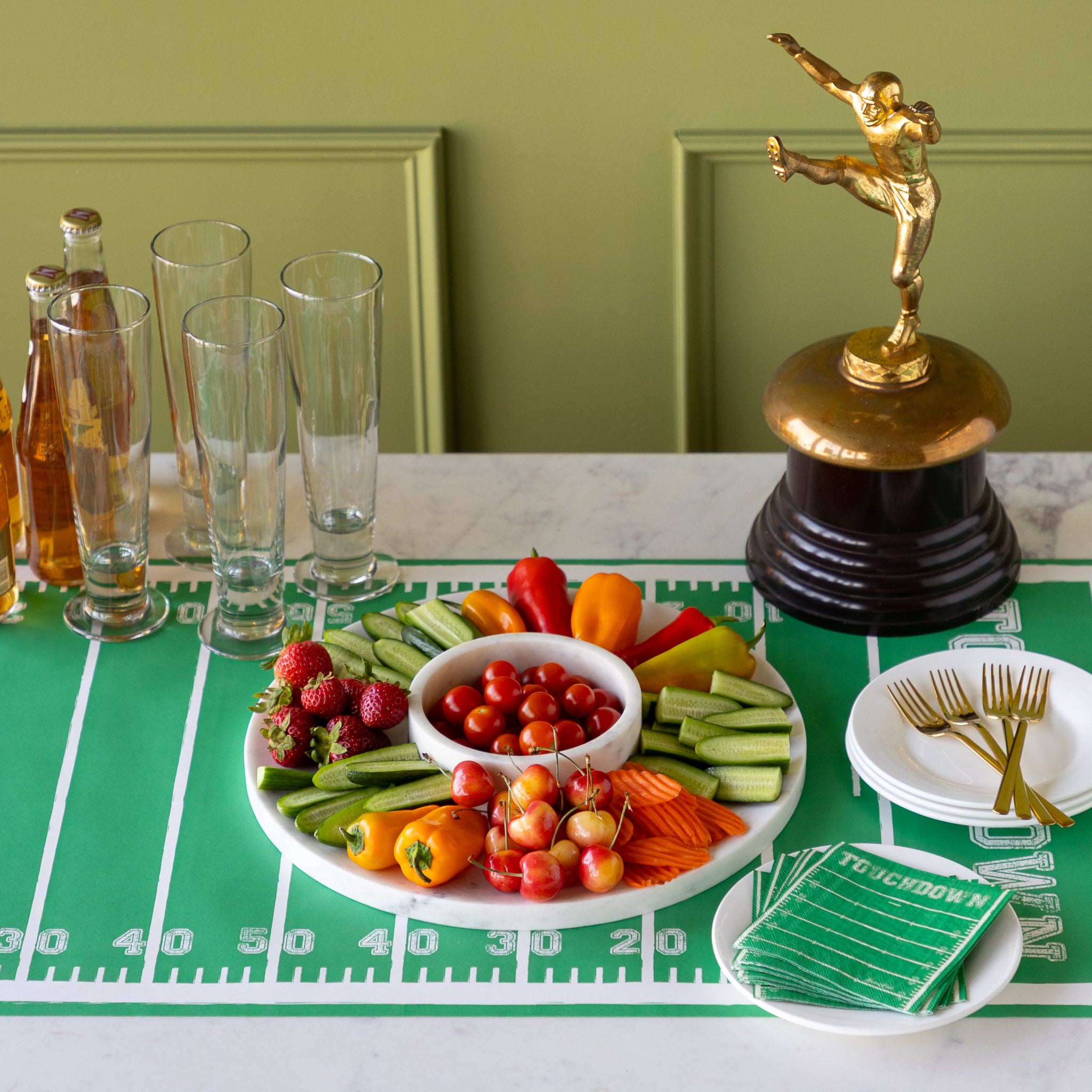 Marble Chip and Dip Server with fruits and veggies atop, Touchdown Cocktail Napkins, a gold trophy, and glasses, plates and forks on the Touchdown Runner.
