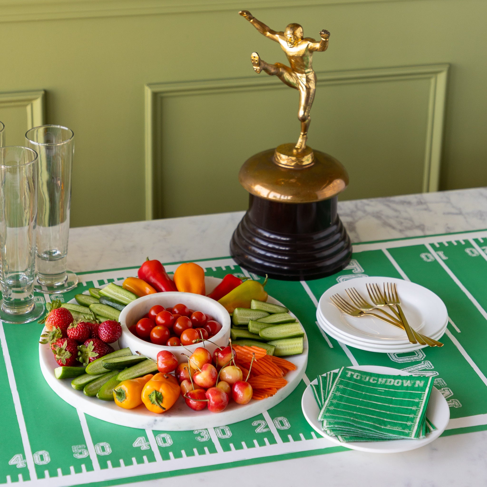 Marble Chip and Dip Server with fruits and veggies atop, Touchdown Cocktail Napkins, a gold trophy, and glasses, plates and forks on the Touchdown Runner.