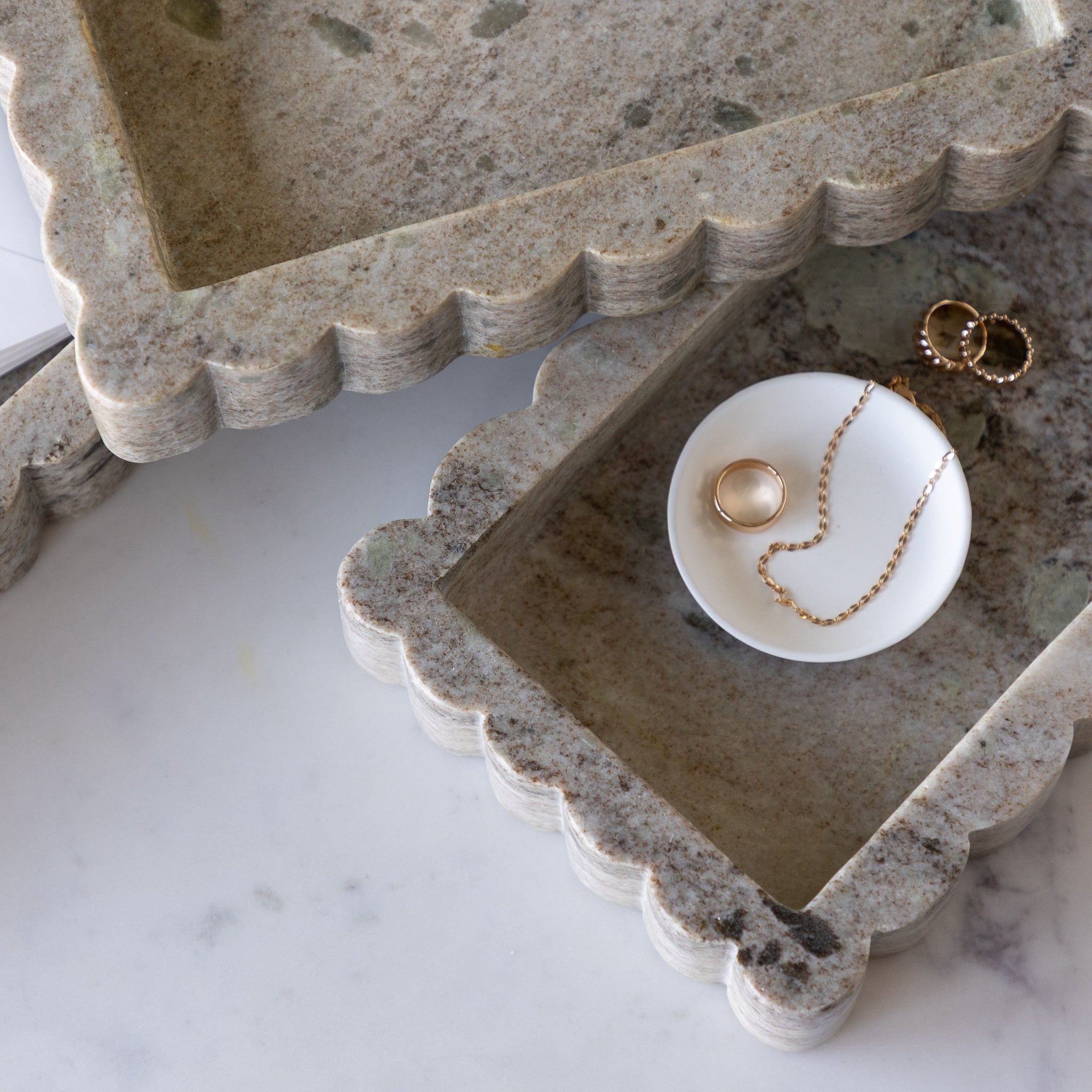 Intricate Scallop Marble Trays on a marble surface with a white dish containing gold jewelry in one.