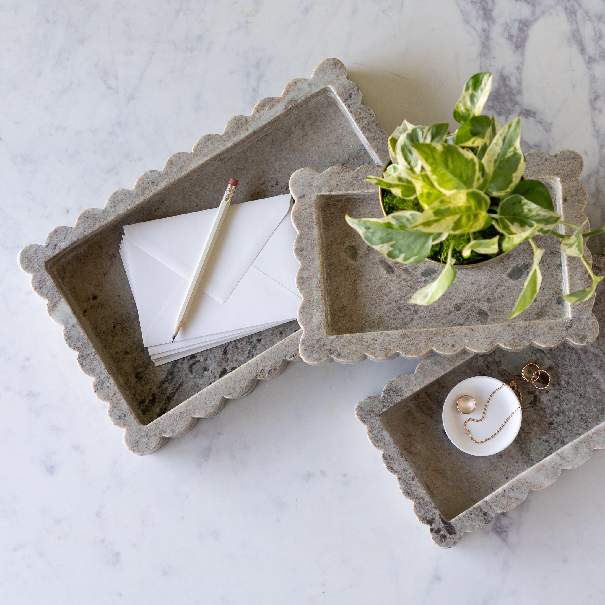 Intricate Scallop Marble Trays in 3 sizes with a potted plant in the small, trinket dish with jewelry in the medium and envelopes and a pencil in the large.