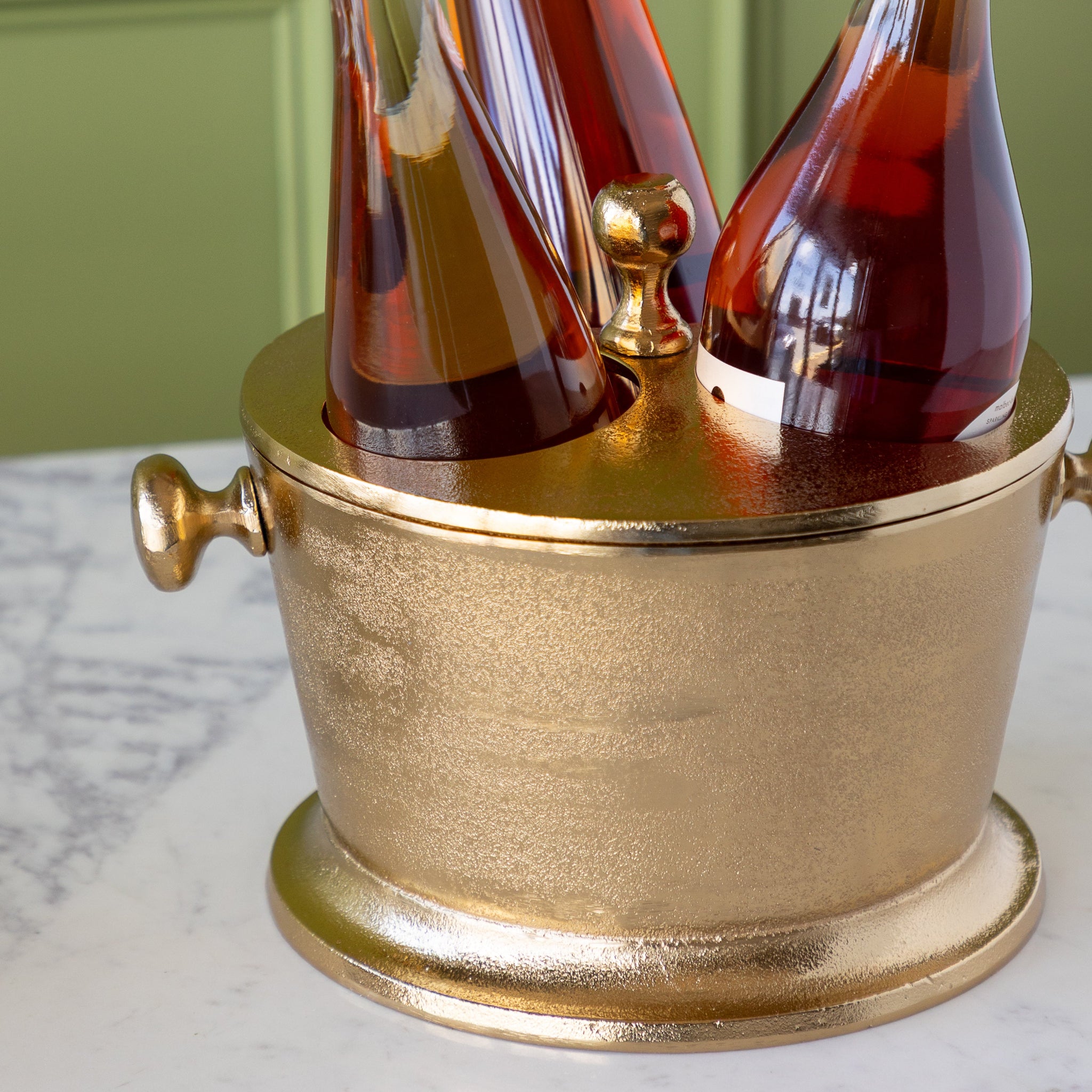 Gold Raw Aluminum Bottle Holder with three wine bottles on a marble surface.