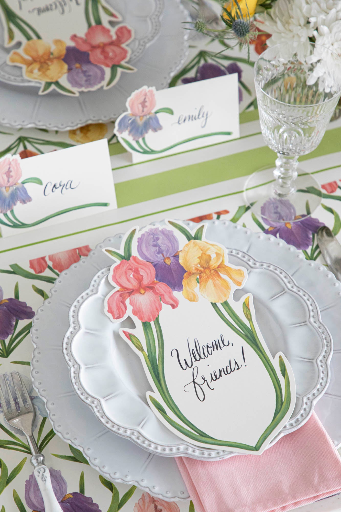 An elegant floral place setting featuring an Iris Table Card with &quot;Welcome, friends!&quot; written on it in beautiful script resting on the plate.