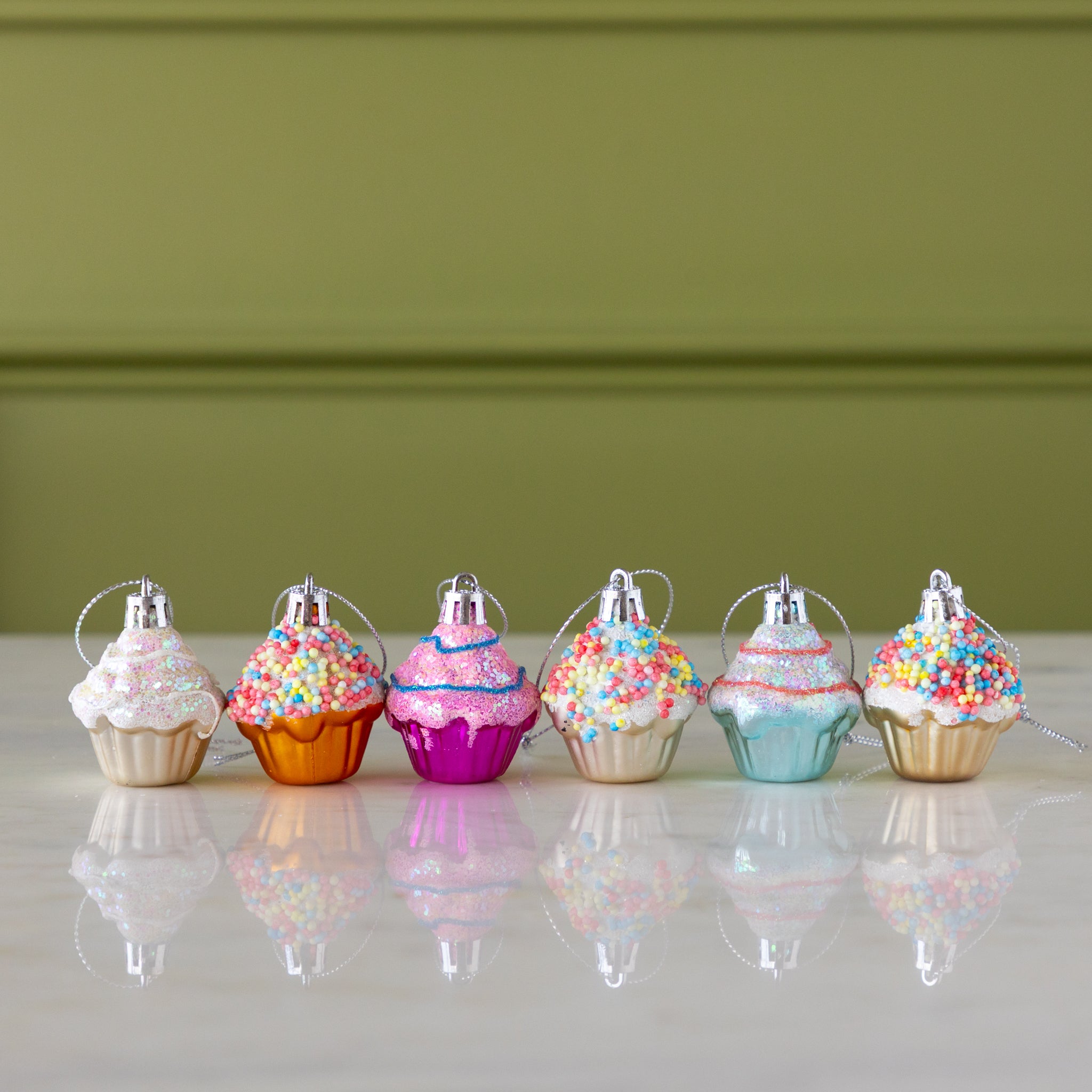 Colorful cupcake-shaped ornaments on a marble surface with a green wall background.