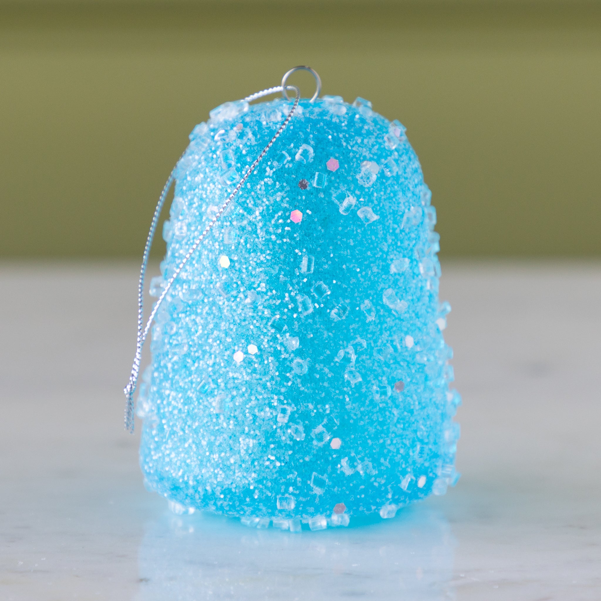 Blue glittery gum drop ornament on a neutral background.