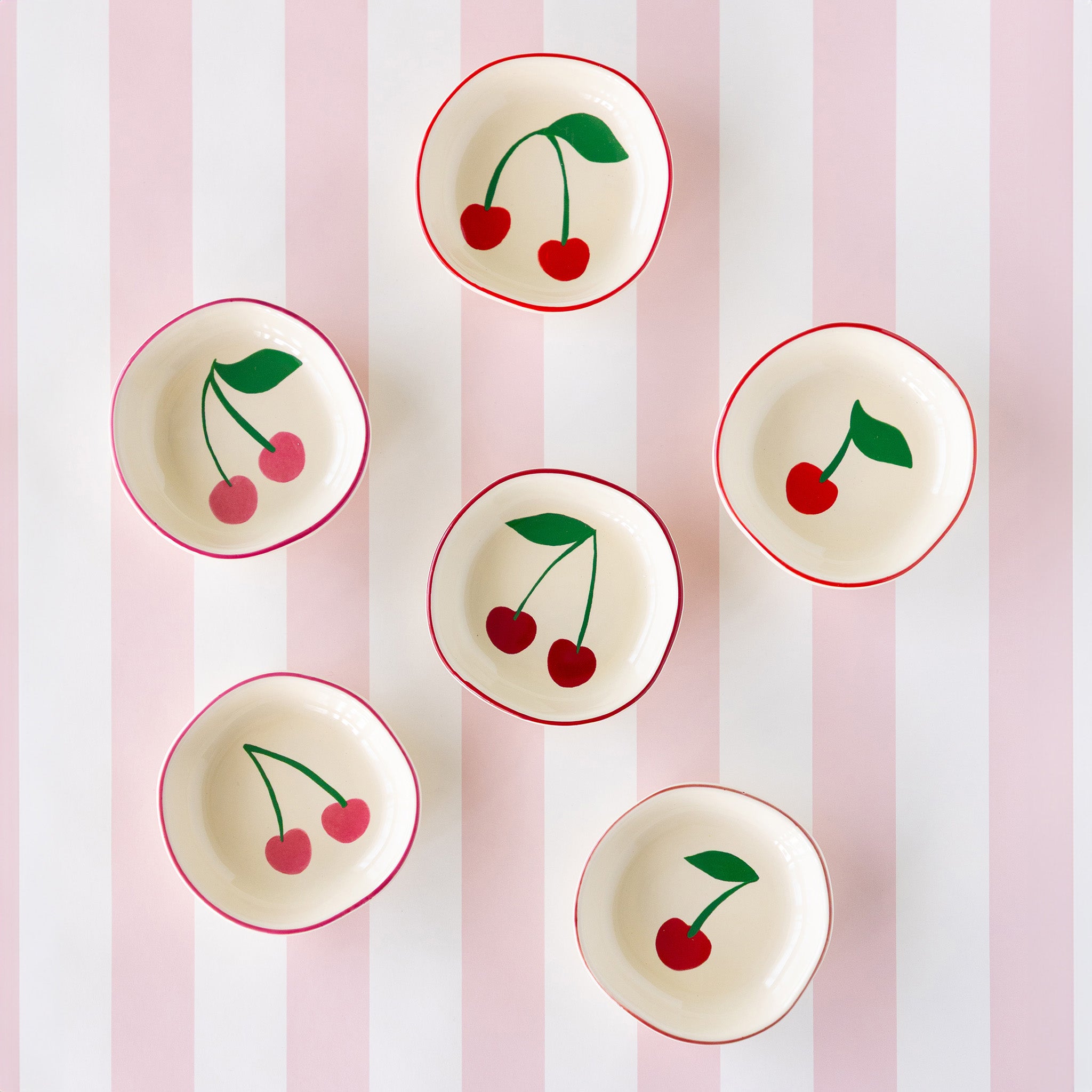 Six ceramic cherry pinch bowls with red rims and charming cherry illustrations inside, arranged on the Pink Classic Stripe Runner.