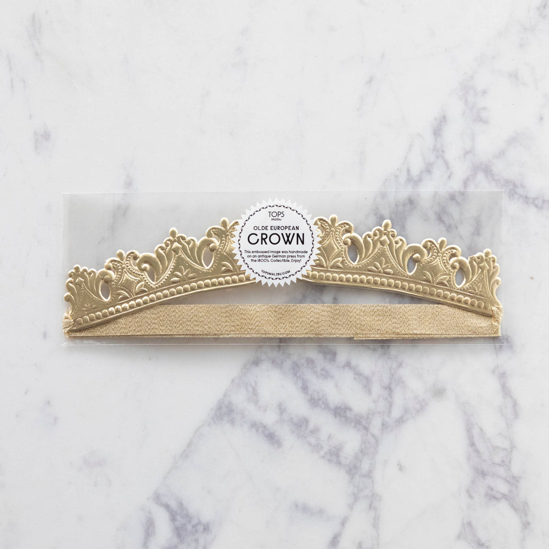 Three Crown Embossed Gold tiaras with a royal touch on a marble table by Tops Malibu.