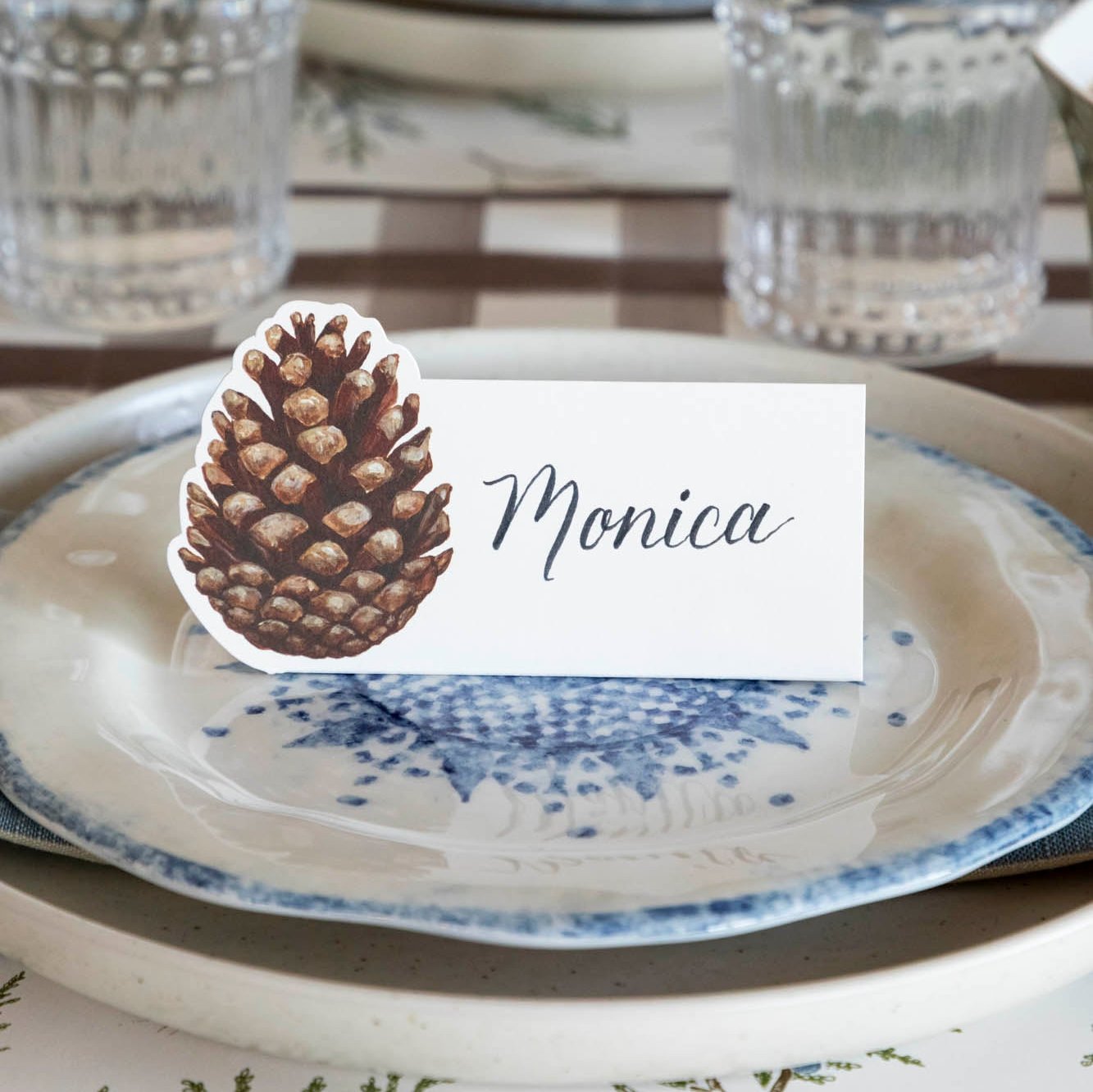 An elegant table setting with a Pinecone Place Card with the name "Moncia" written on it, on top of dinner plates.