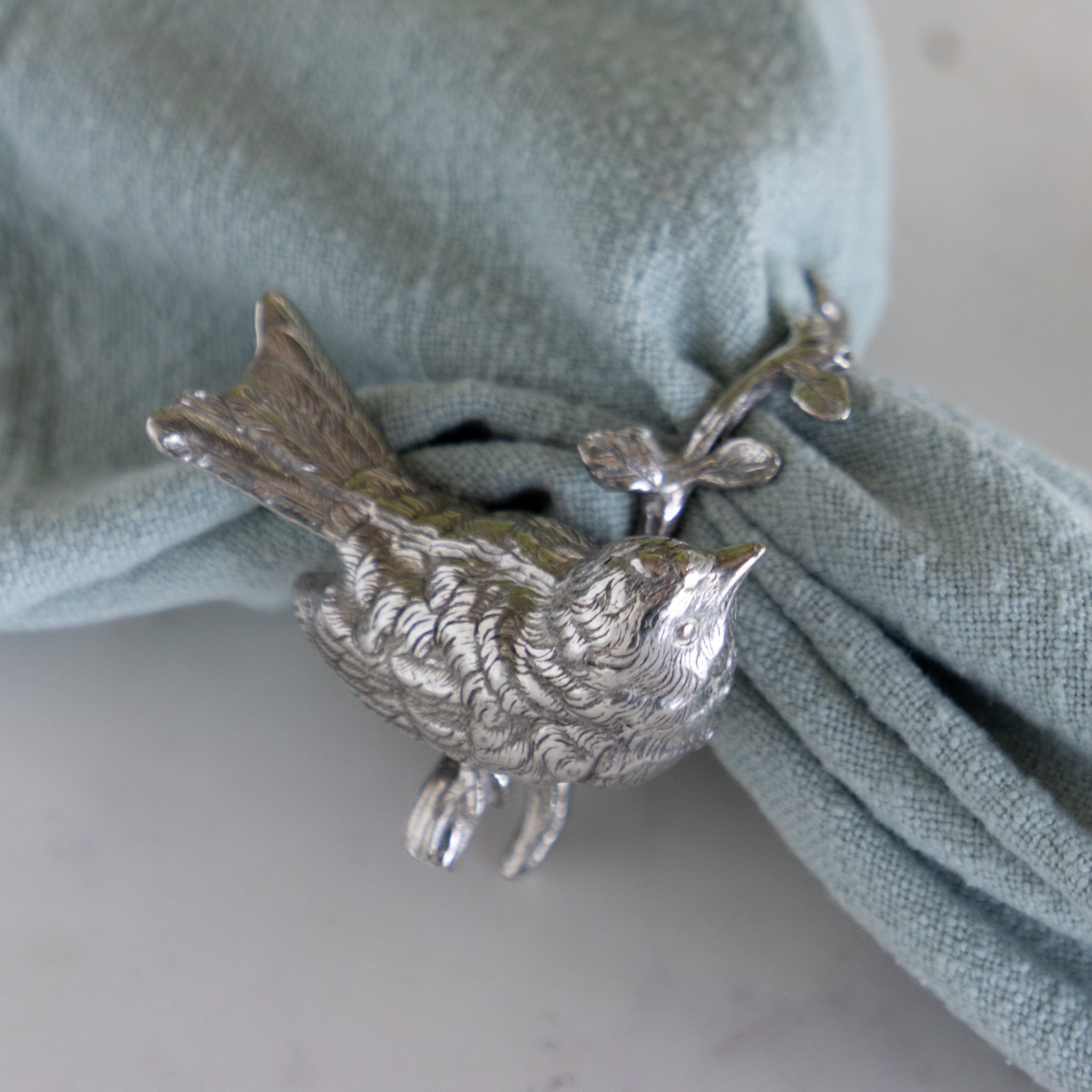 Silver bird-shaped napkin ring on a green napkin.
