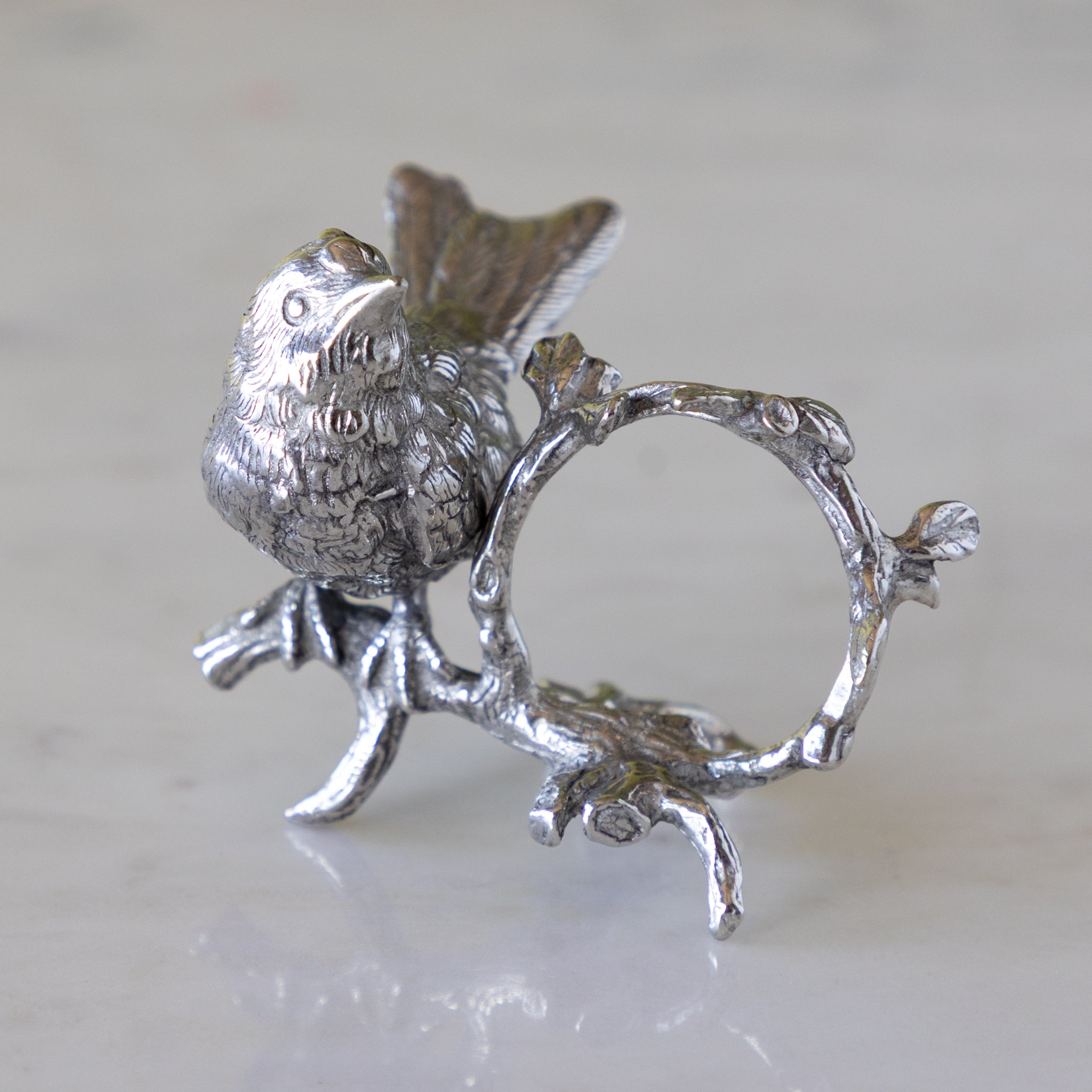 Silver bird on a branch with a circular element, on a light background.