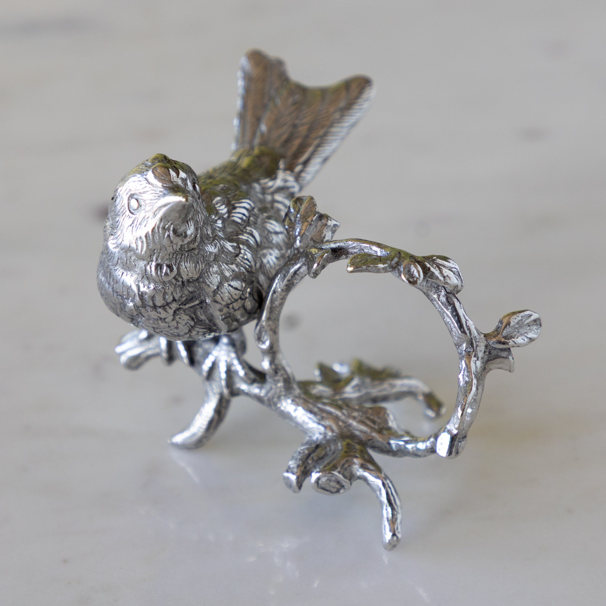 Silver bird a branch with a circular element, on a light background.