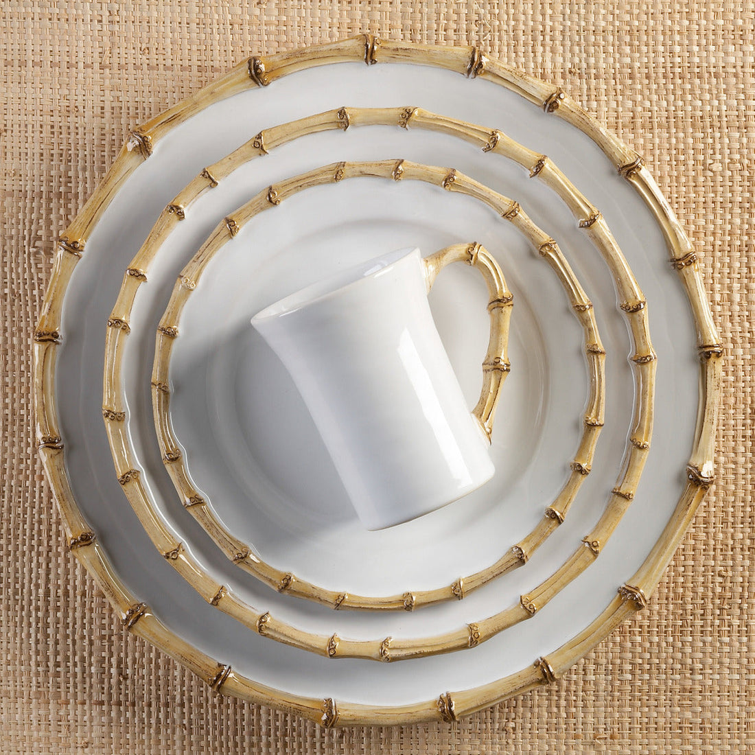 An overhead view of a stack of elegantly designed dishwasher safe Juliska Classic Natural Bamboo dinnerware with a bamboo motif, placed on a textured beige surface.