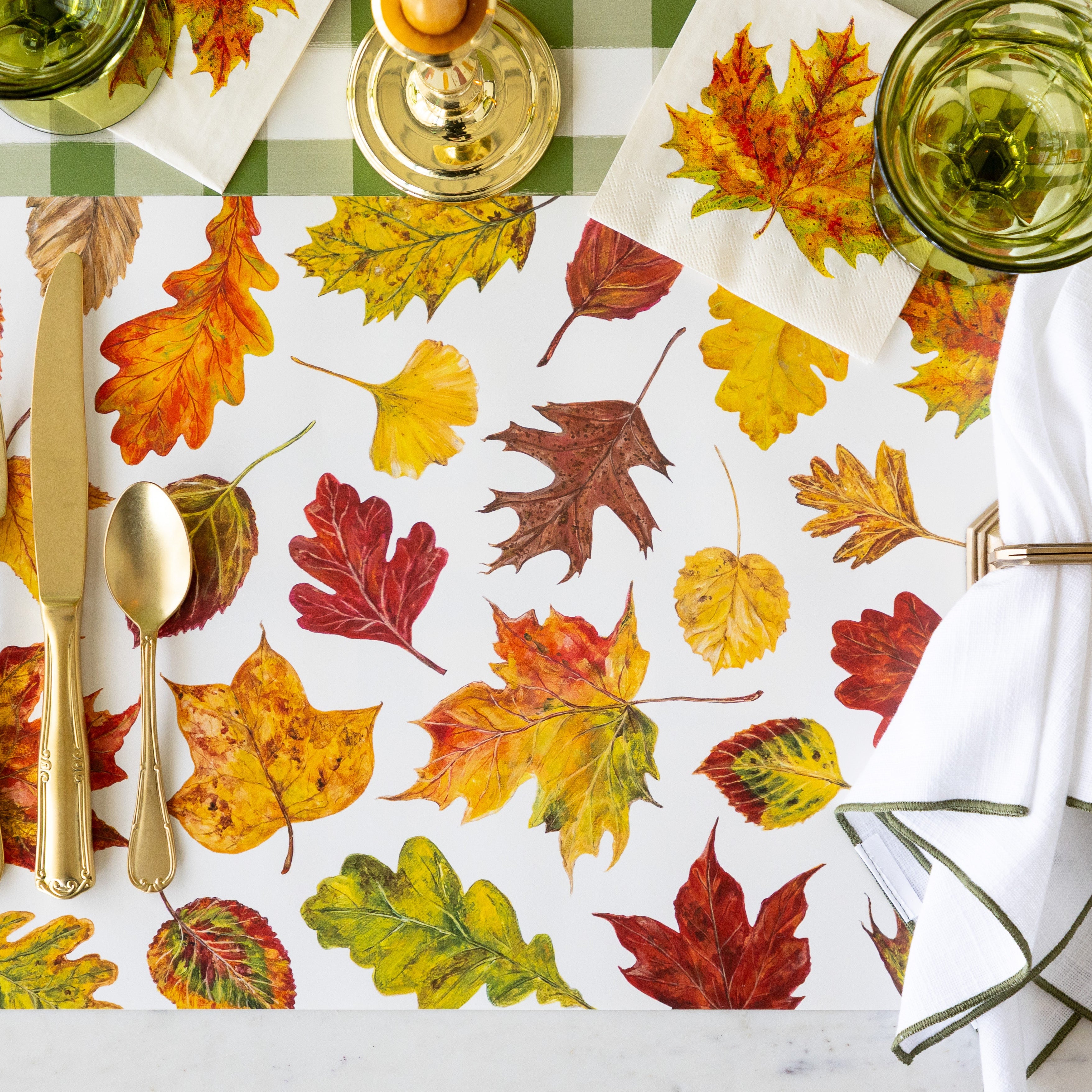 A place setting with no plates featuring the Fall Foliage Placemat under vintage gold flatware, a napkin in a holder, the Fall Foliage Cocktail Napkin under a glass and Moss Green Painted Check Runner underneath.