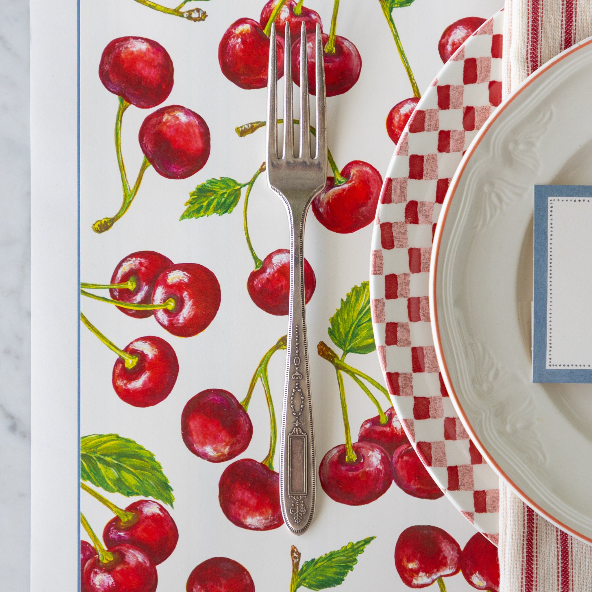 Placemat with cherry design featuring a fork and red and white plates atop.