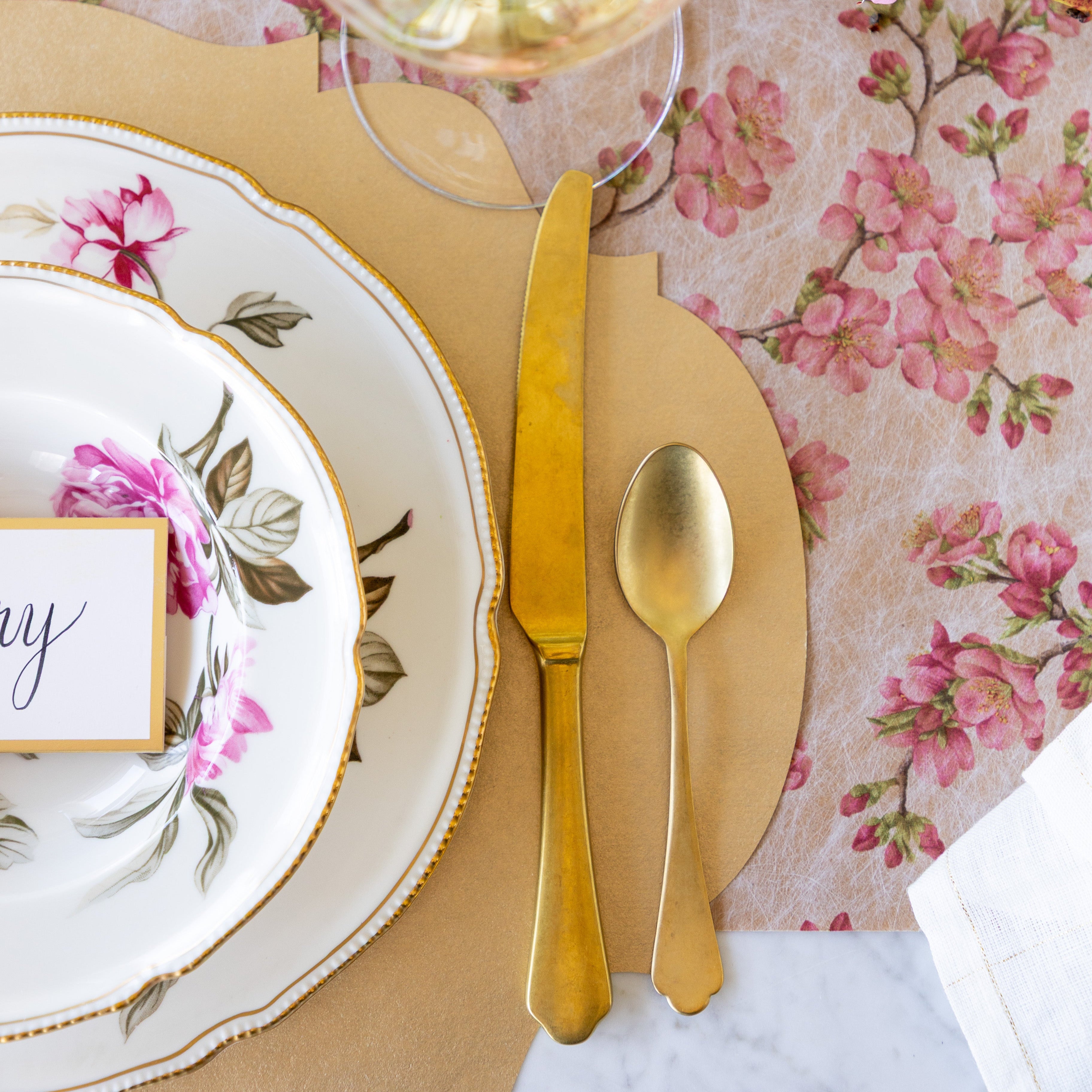 An elegant place setting featuring the Die-cut Gold French Frame Placemat under vintage floral dinnerware, gold flatware, and Cherry Blossom Runner underneath.
