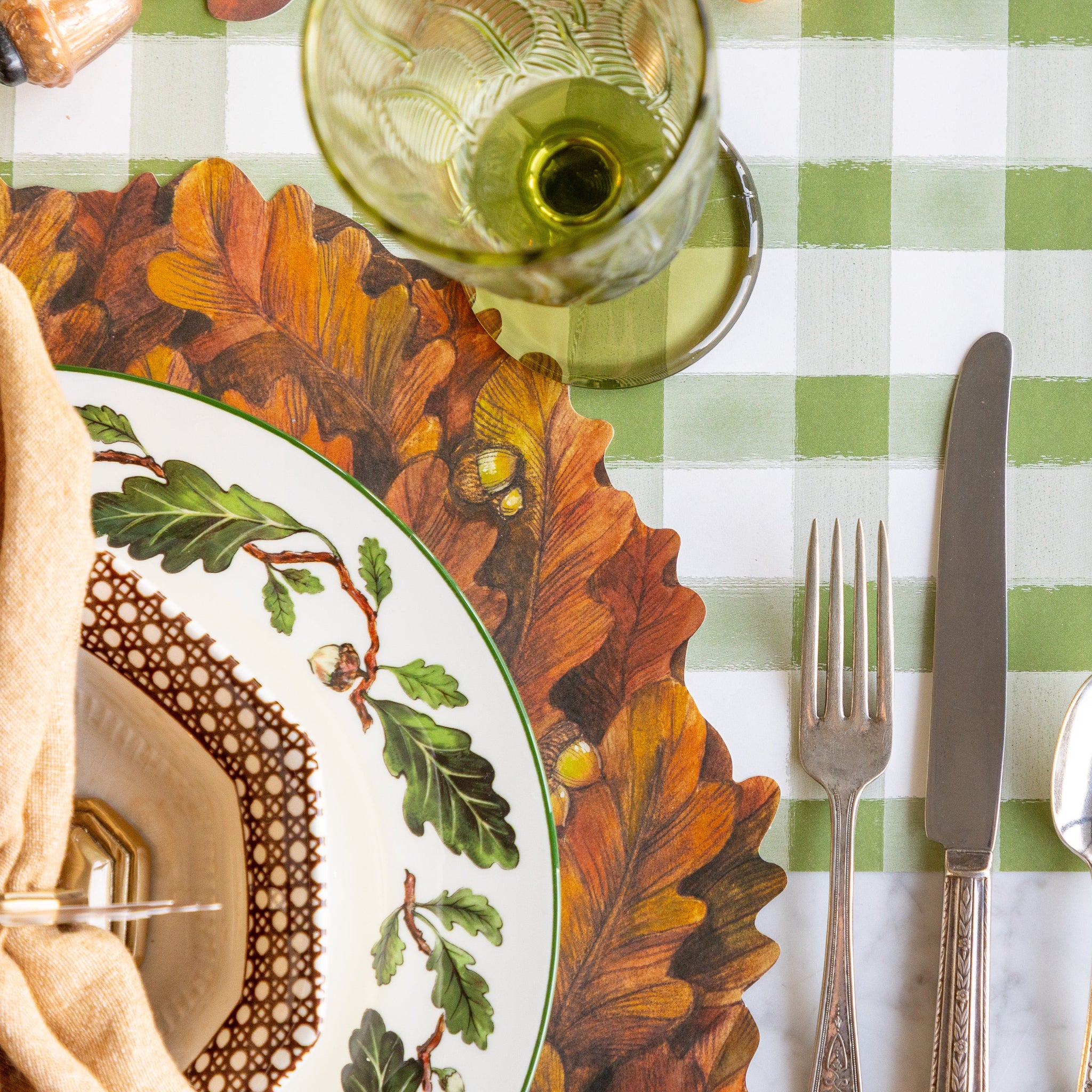 Table setting with the Die-cut Autumn Wreath Placemat, vintage plate with acorns and leaves, silverware and a green glass on the Moss Painted Check Runner.