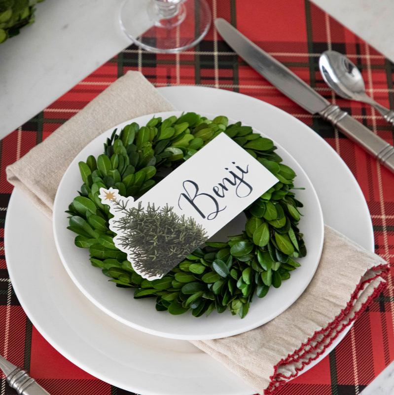 An elegant Christmastime place setting, featuring a Christmas Tree Place Card labeled "Benji" laying flat on the plate.