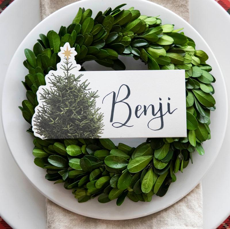 Top-down view of an elegant Christmastime place setting, featuring a Christmas Tree Place Card labeled "Benji" laying flat on the plate.