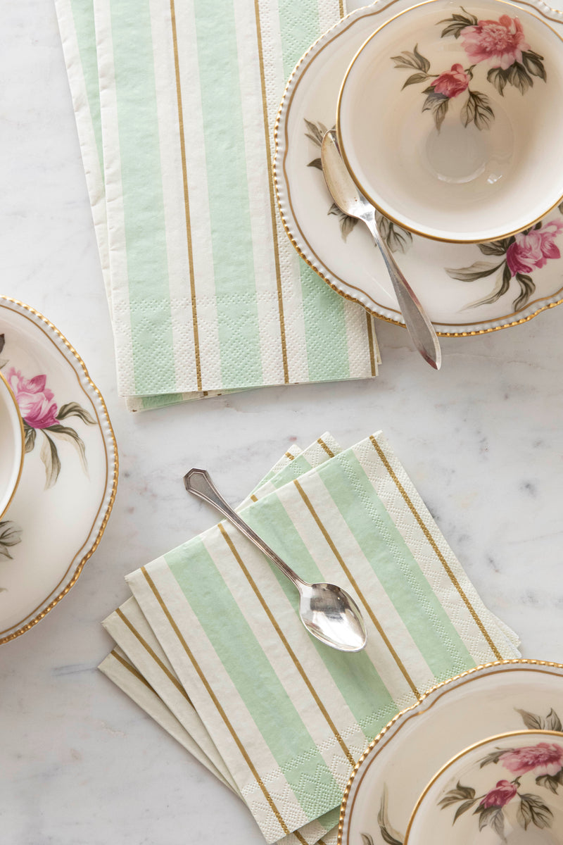 A table setting with Seafoam &amp; Gold Awning Stripe Napkins by Hester &amp; Cook, accompanied by teacups and saucers and a spoon.