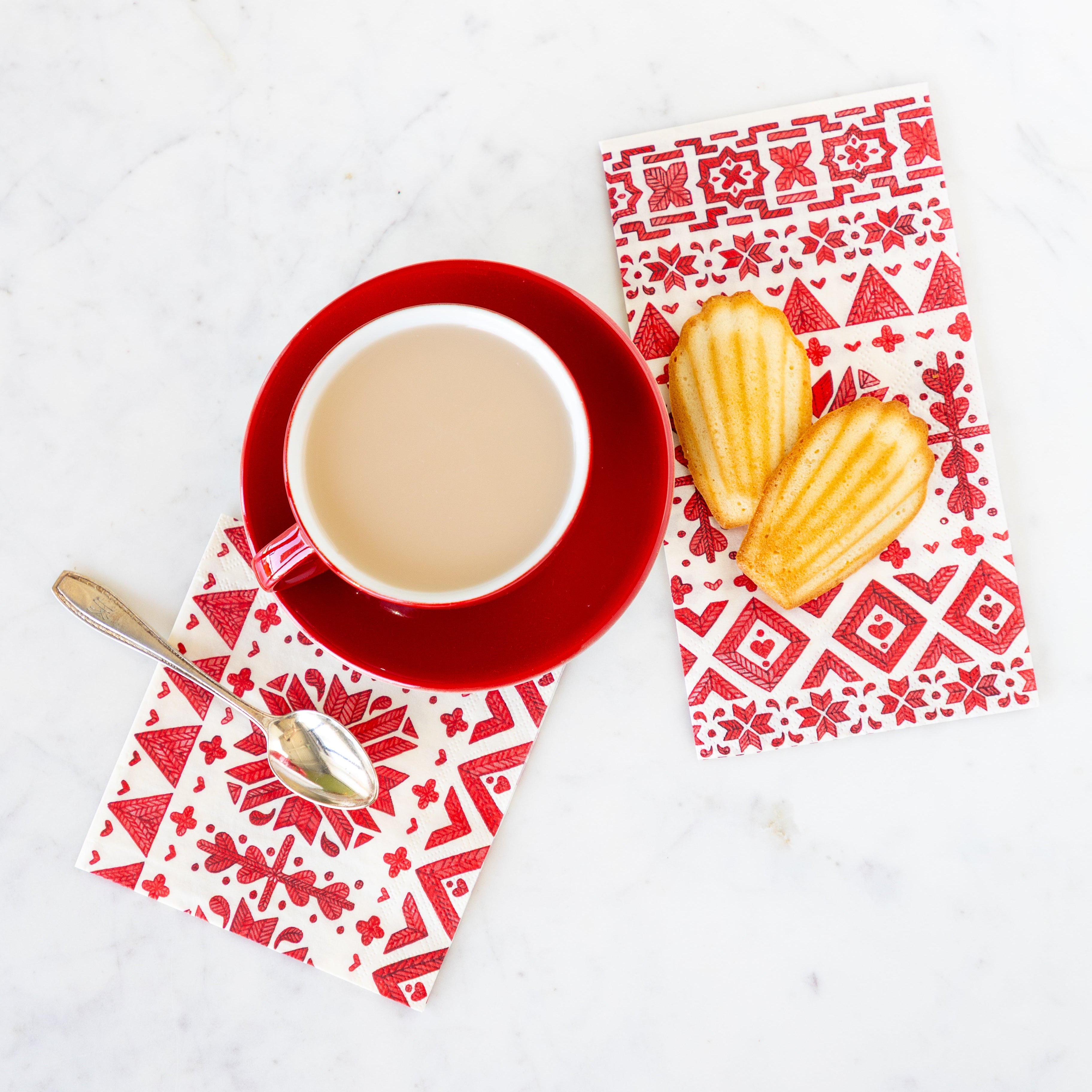 Fair Isle Cocktail and Guest Napkins on a table––a red saucer and mug with coffee and a spoon on the cocktail and Madelines on the guest.