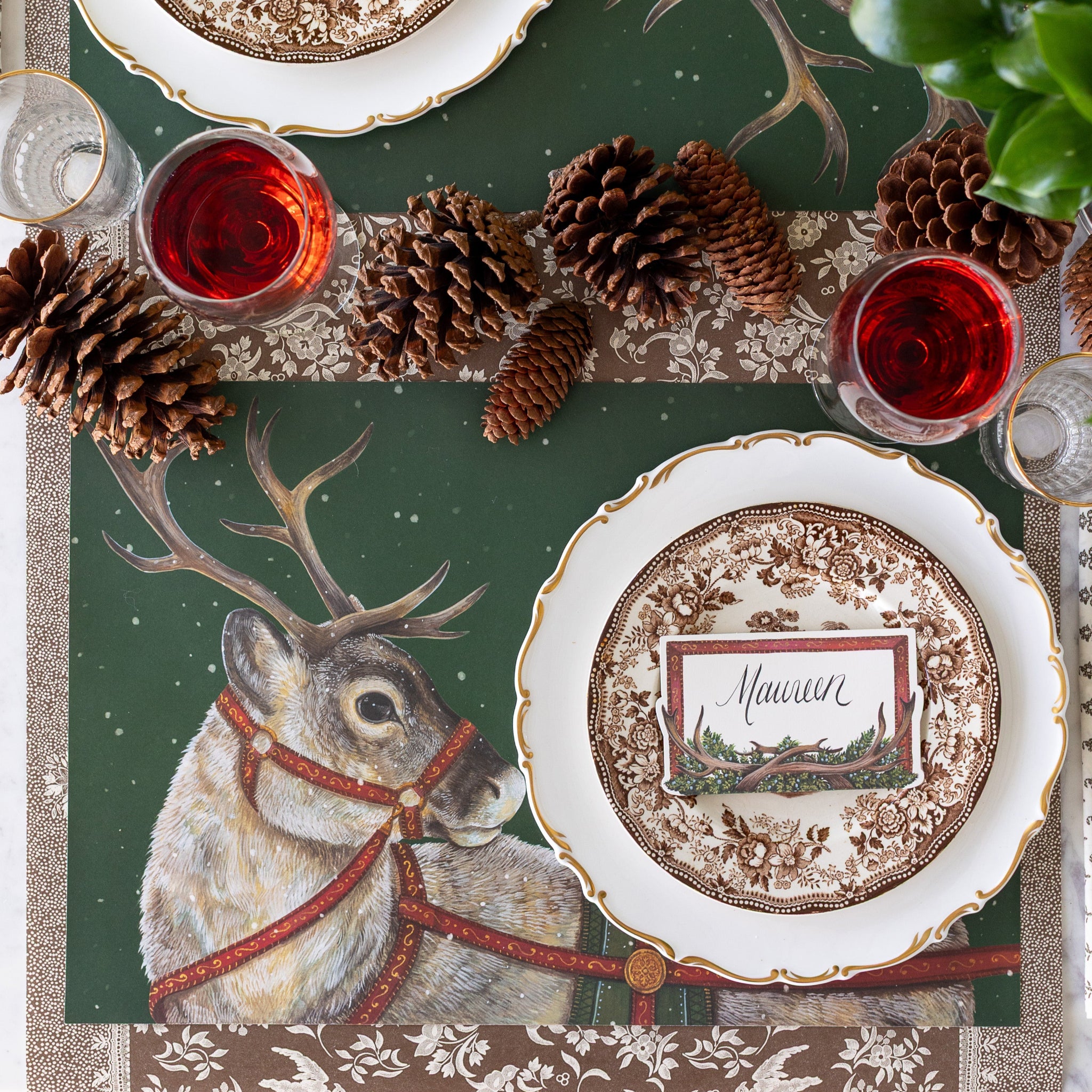 Decorative table setting with the Holiday Reindeer Placemat, Antler Garland Table Card, pine cones and Antler Frame Place Cards on the Brown Regal Peacock Runner.