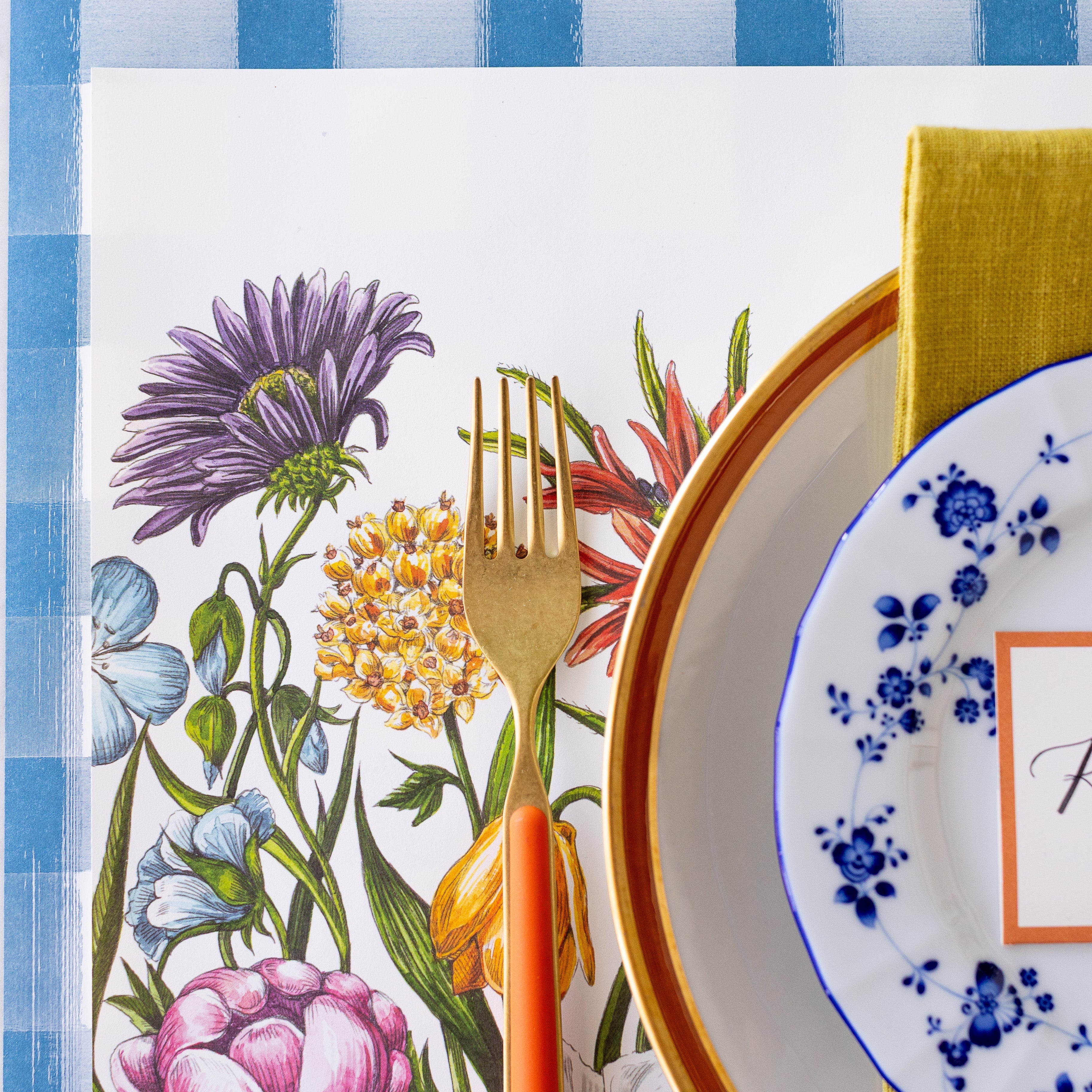A spring place setting with a gold and orange fork on the Wildflower Meadow Placemat.
