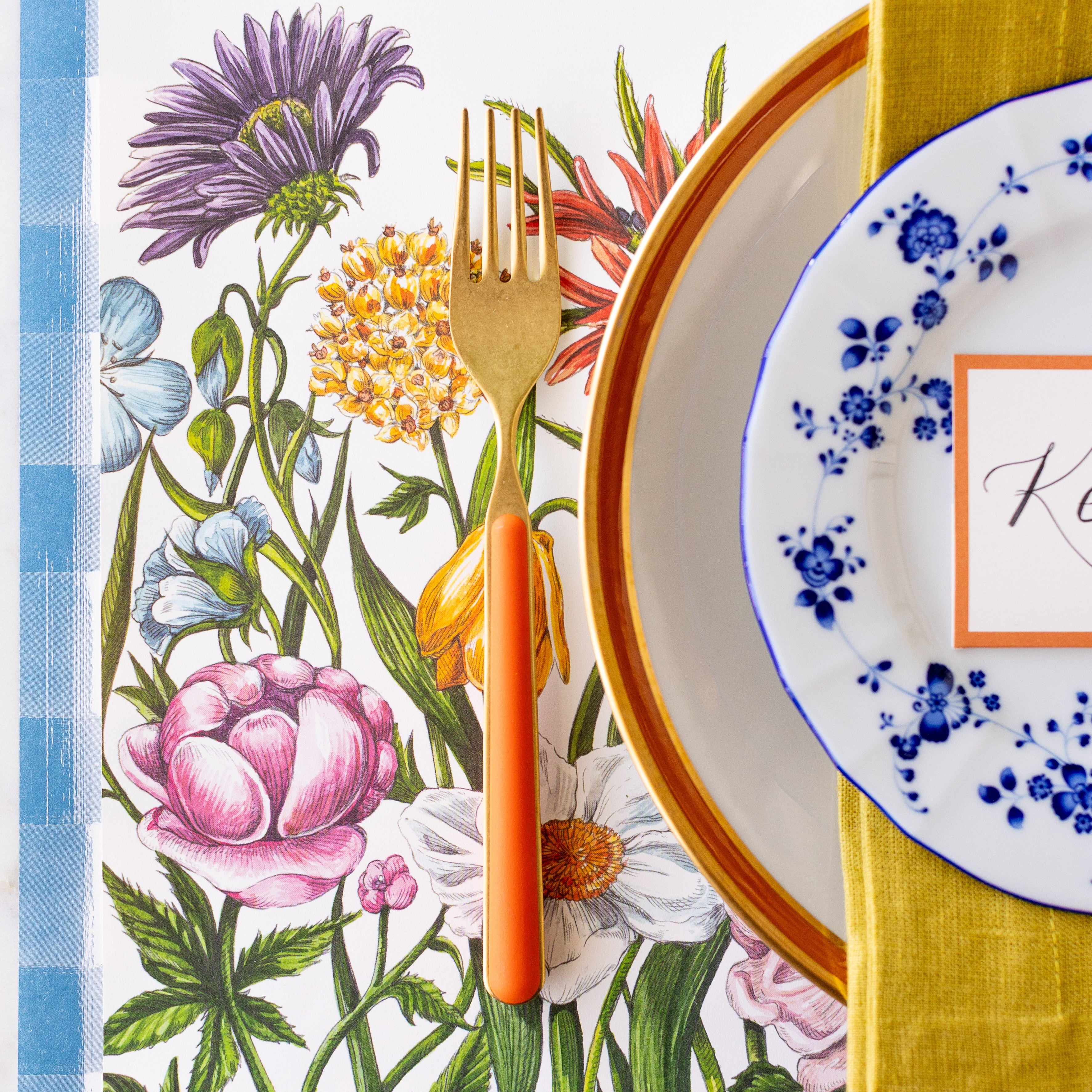 A spring place setting with a gold and orange fork on the Wildflower Meadow Placemat.