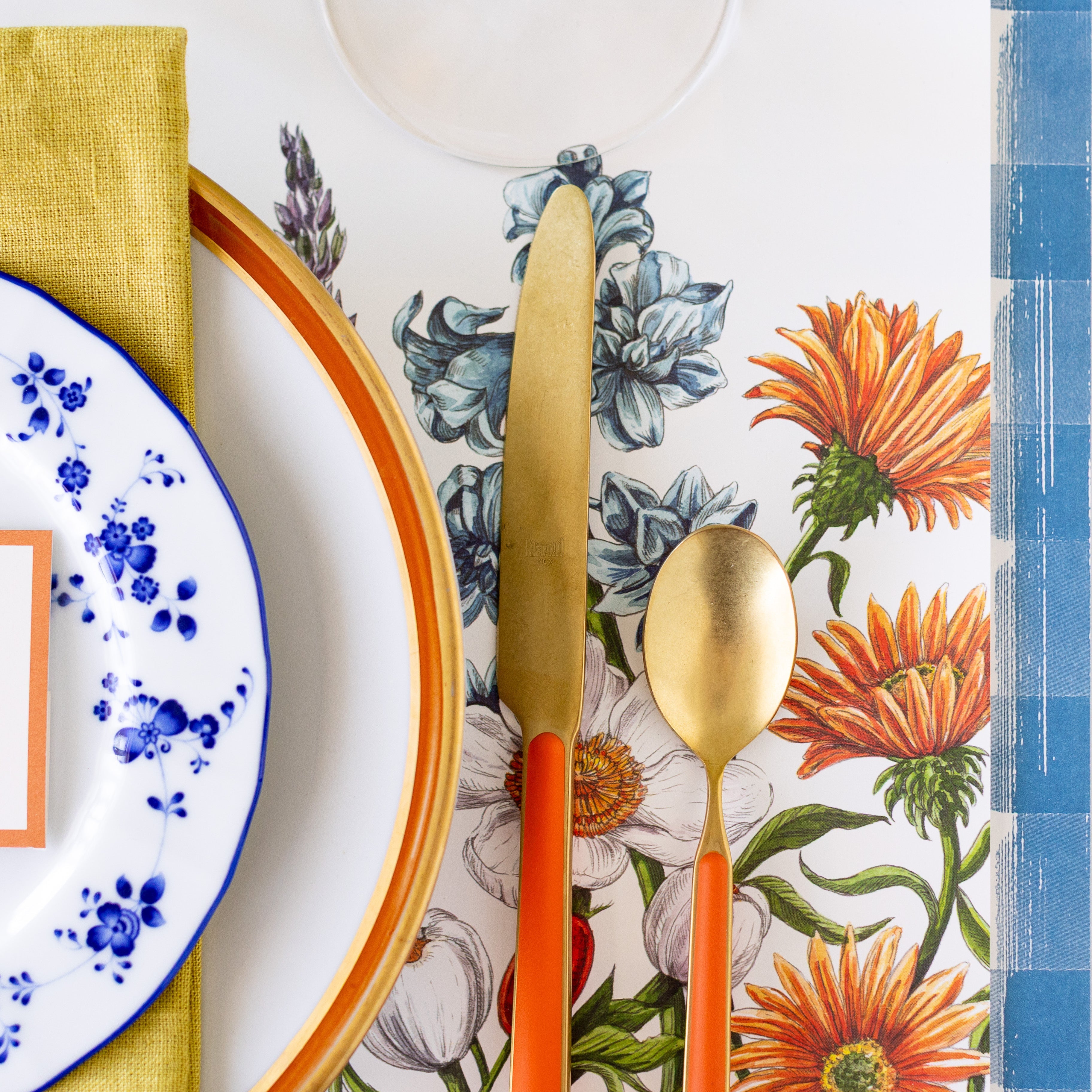 A close up of the Wildflower Meadow Placemat with orange and gold flatware on top.