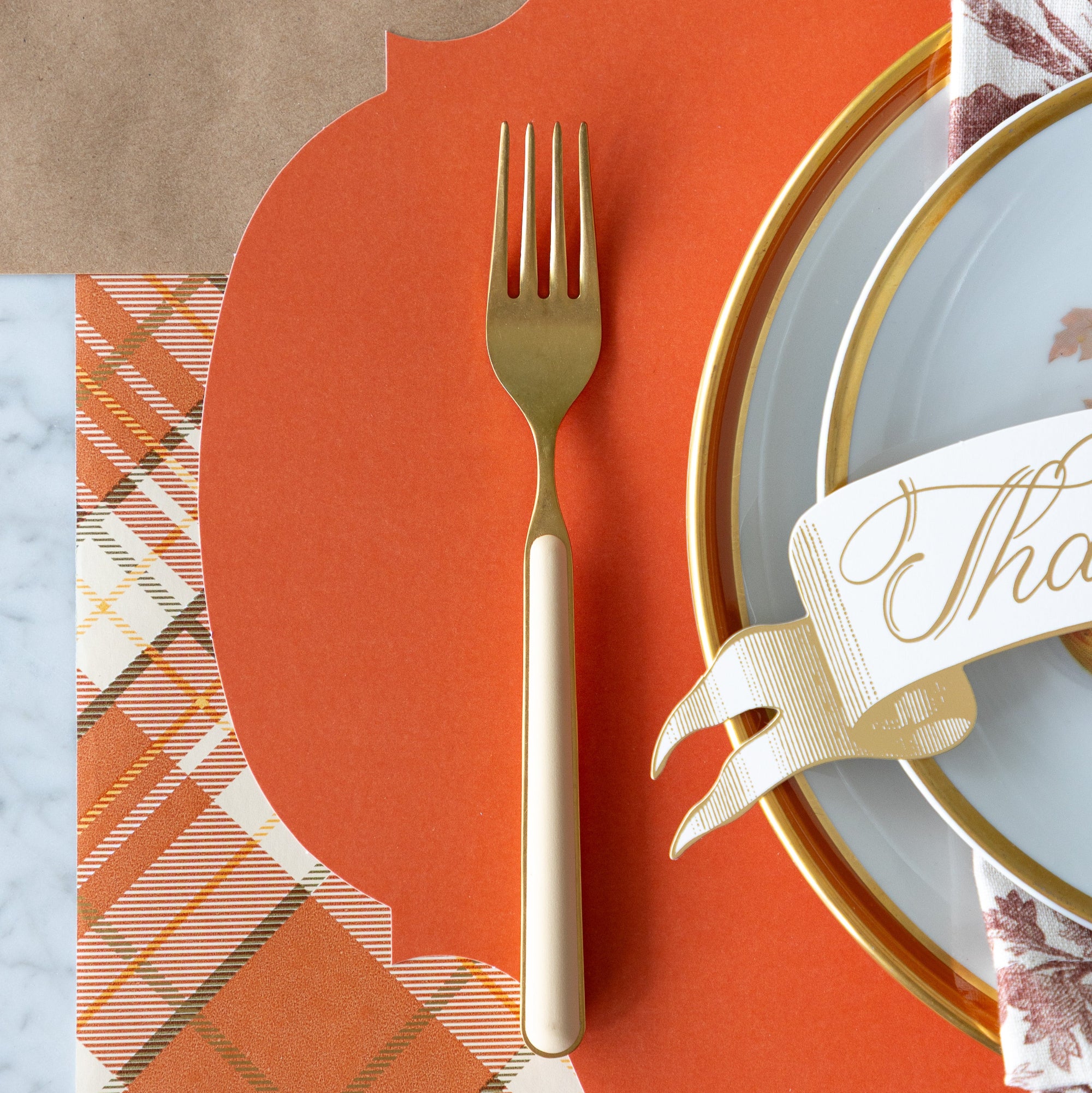 The Die-cut Orange French Frame Placemat under a place setting with vintage dinnerware, and a gold fork with a cream handle on the Orange Plaid Runner.