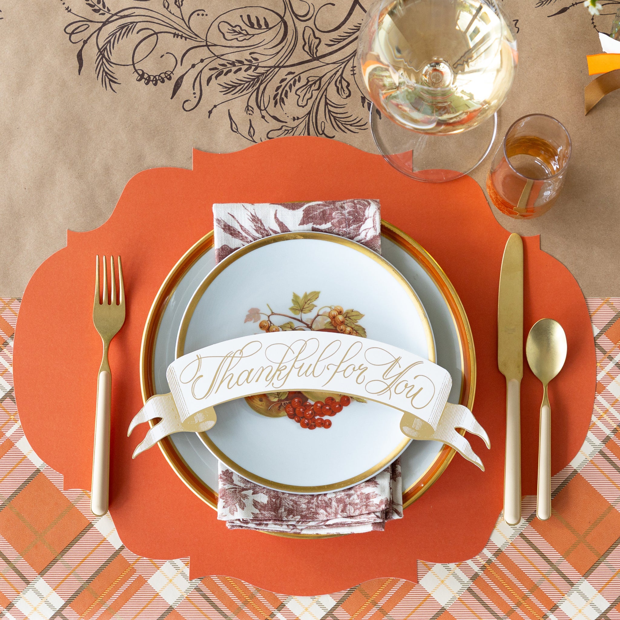 Thanksgiving table setting with Die-cut Orange French Frame Placemat, vintage dinnerware with the Thankful For You Table Accent atop, gold cutlery, and decorative napkin on the Orange Plaid Runner.