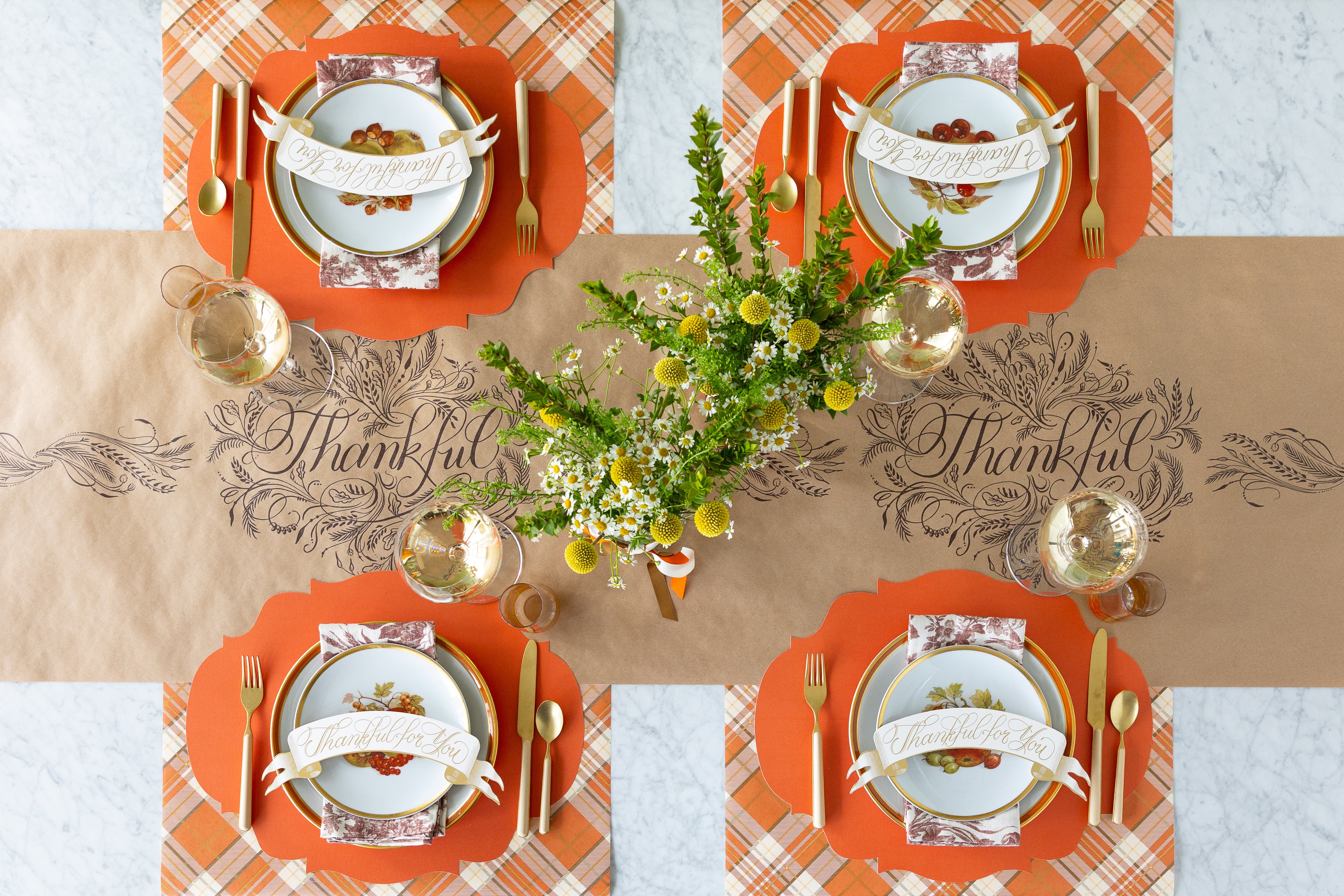 A fall table setting featuring the Die-cut Orange French Frame Placemats, Thankful For You Banner Table Accents, floral napkins and Kraft Thankful and Orange Plaid Runners.
