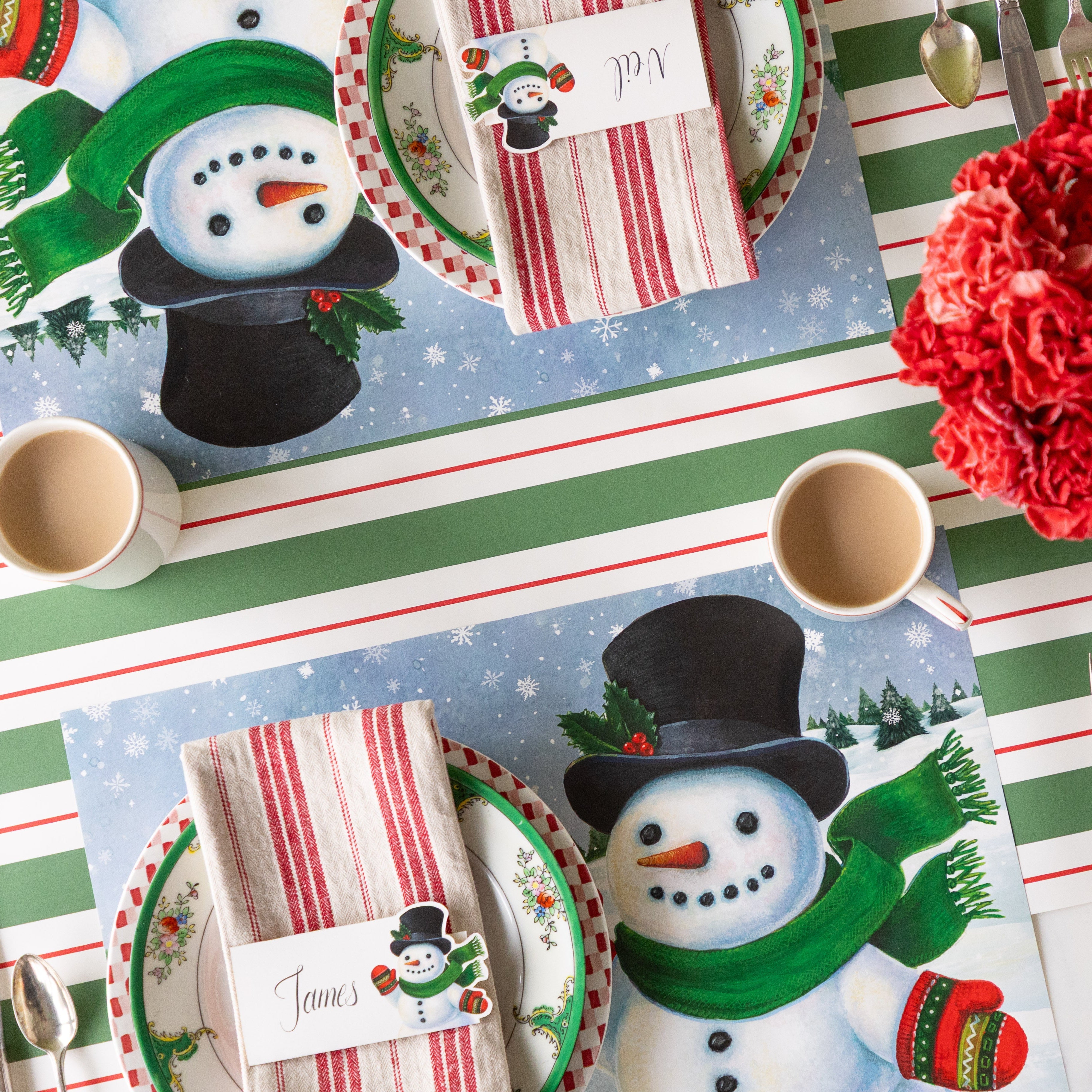 Two place settings with the Jolly Snowman Placemats, red stripe napkins and Jolly Snowman Place Cards on top, arranged on the Green & Red Awning Stripe Runner.