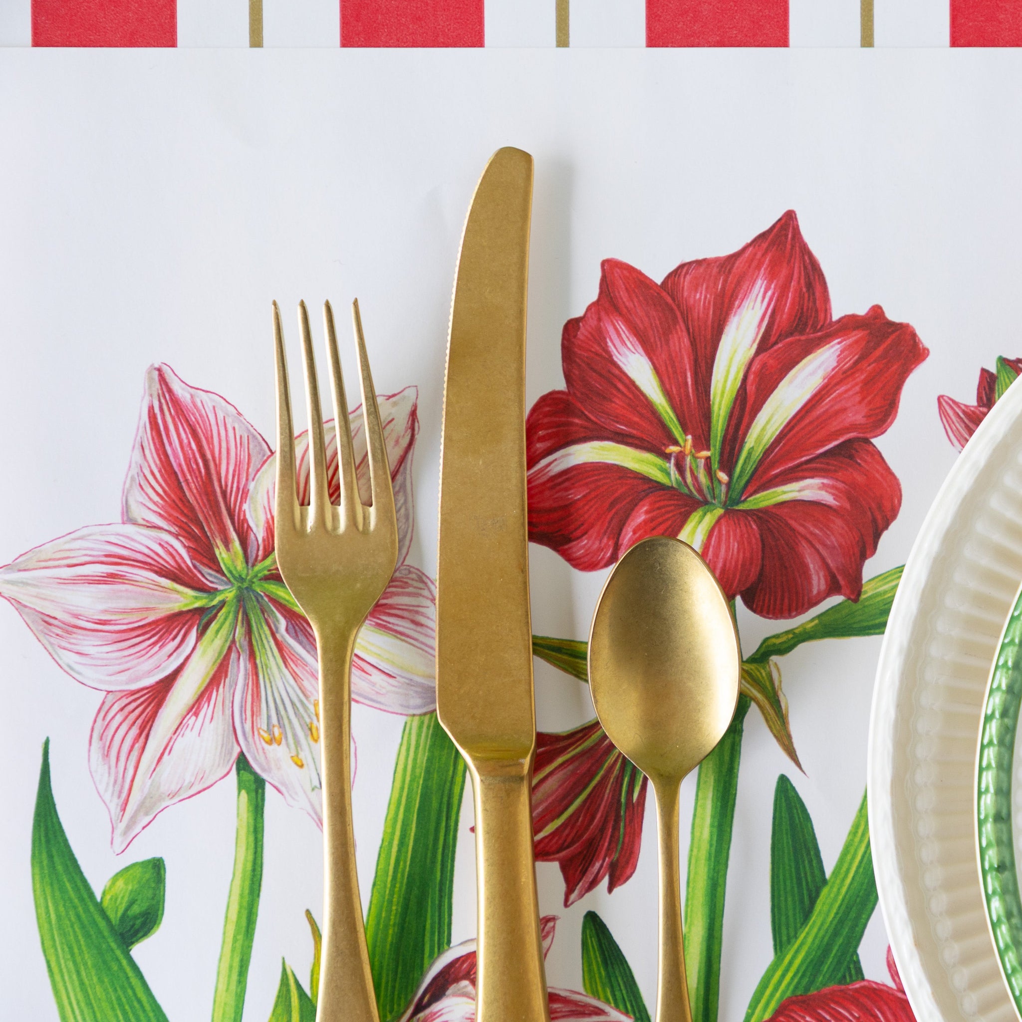 A close up of the Amaryllis Blooms Placemat with gold flatware atop.