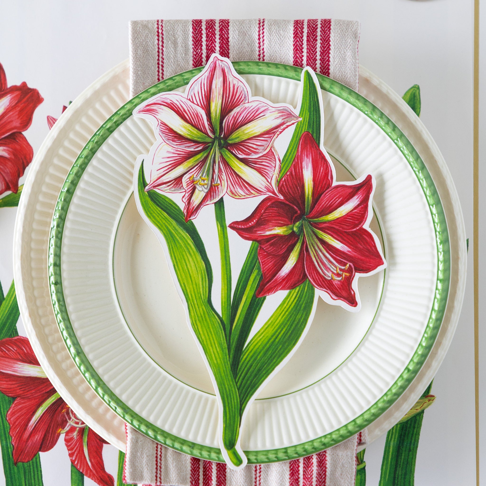 The Amaryllis Table Accent atop dinner plates with a red-and-white striped napkin in between, on the Amaryllis Blooms Placemat.
